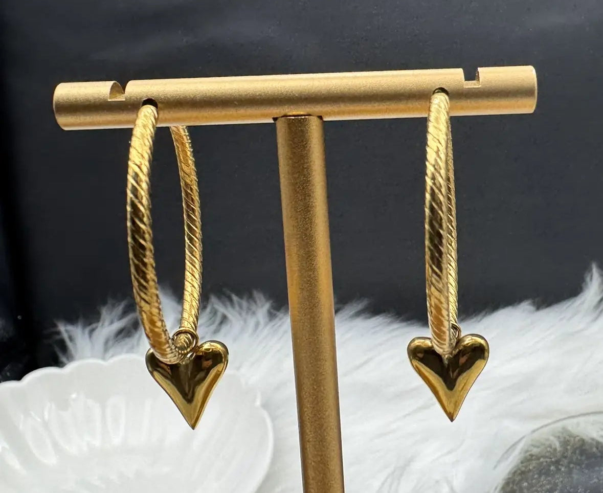 Gold heart-shaped earrings on a gold stand with a dark background