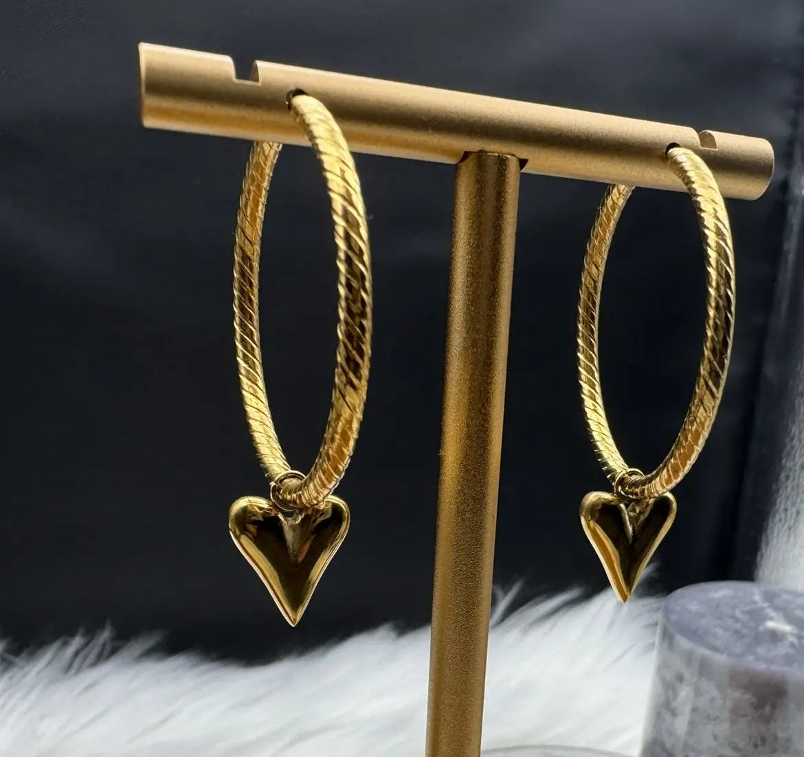 Gold heart hoop earrings on a gold stand with a black and silver background