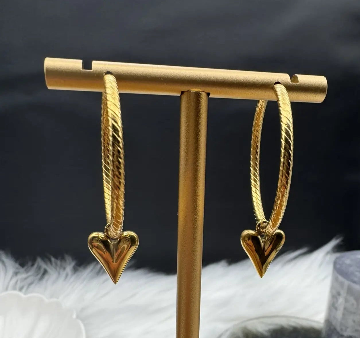 Gold heart-shaped earrings on a gold stand with a black background