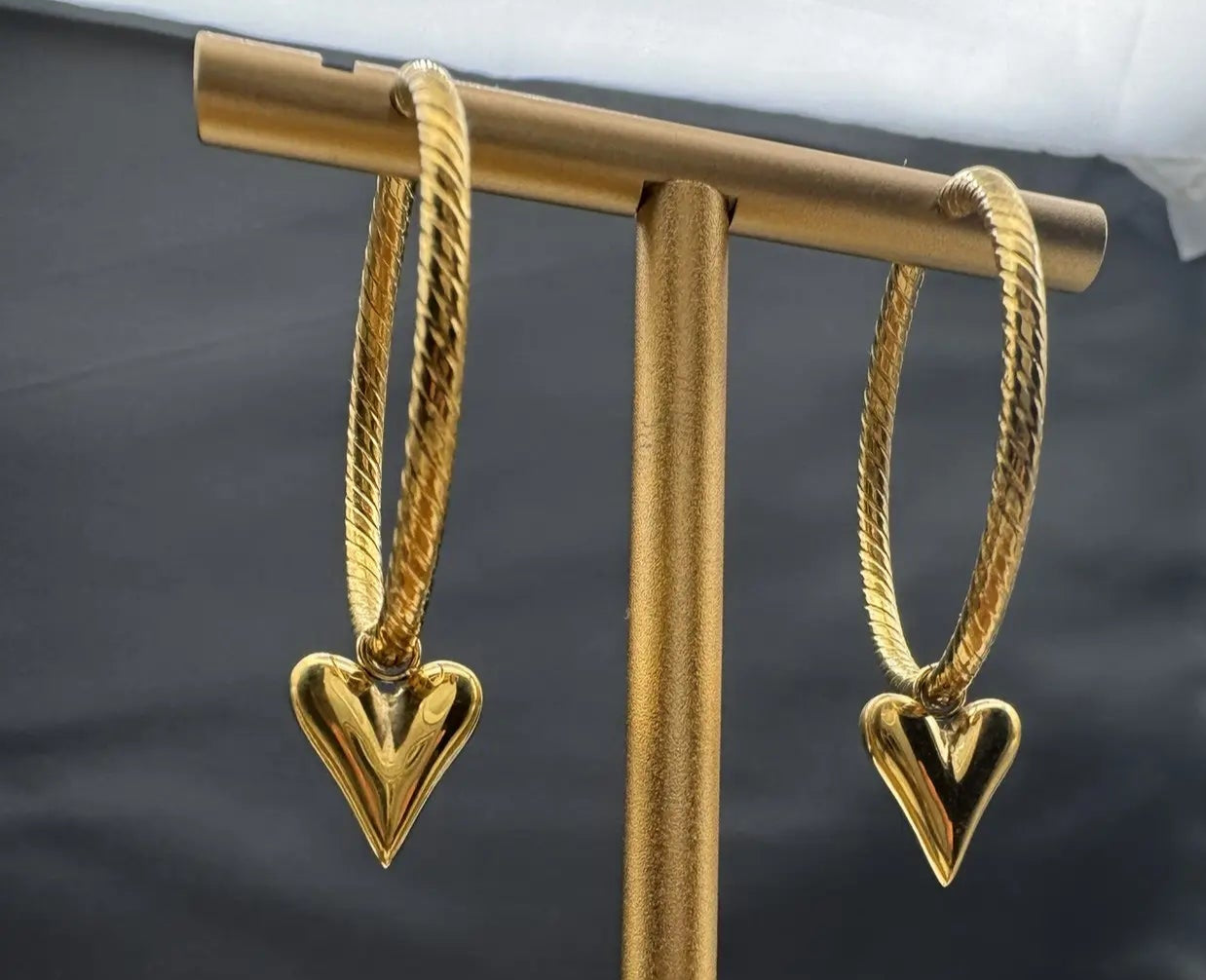 Gold heart-shaped earrings on a gold stand with a black background