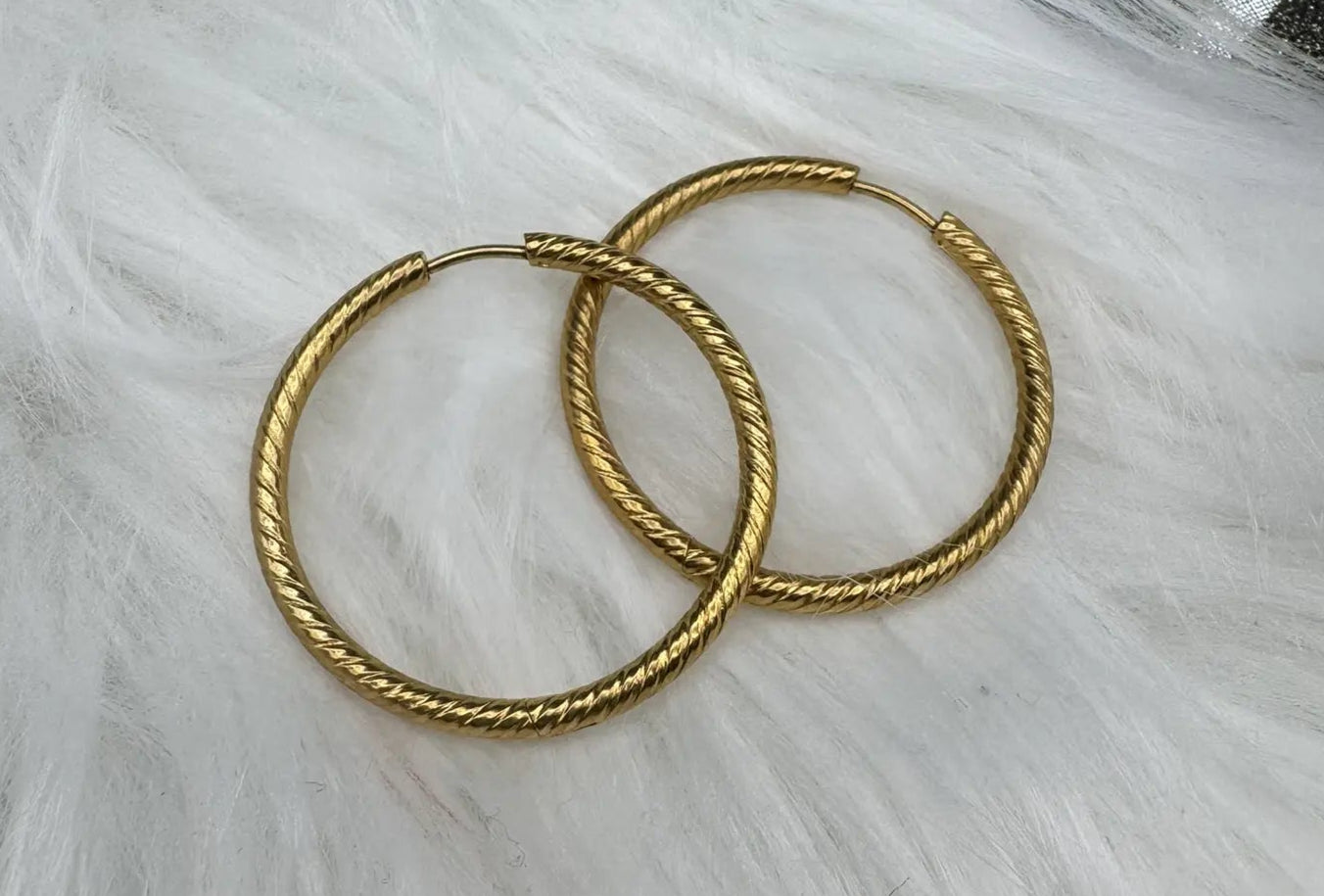 Gold plated hoop earrings on a white furry surface