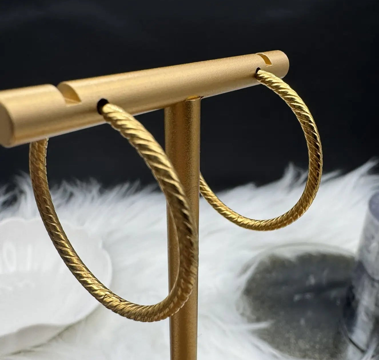 Gold hoop earrings on a gold stand with a black background