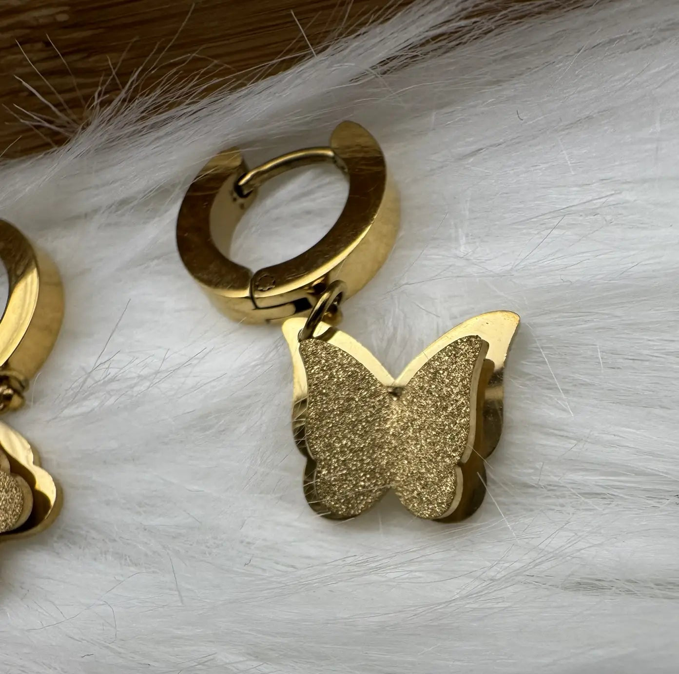 Gold plated hanging shimmering butterfly earrings on a golden stand and black background