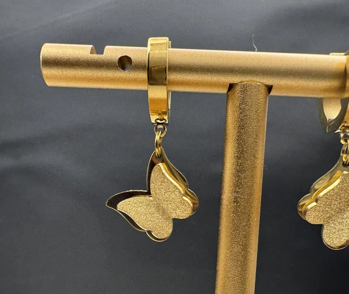 Gold plated butterfly earrings on a gold stand against a dark background