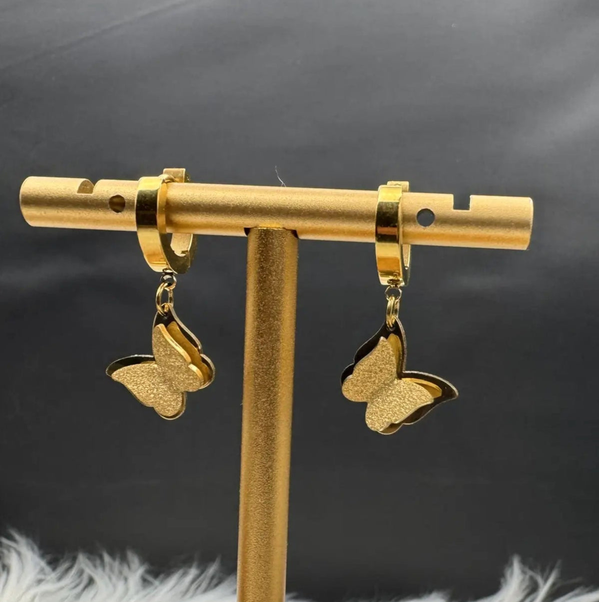 Gold plated butterfly earrings on a stand with a black background