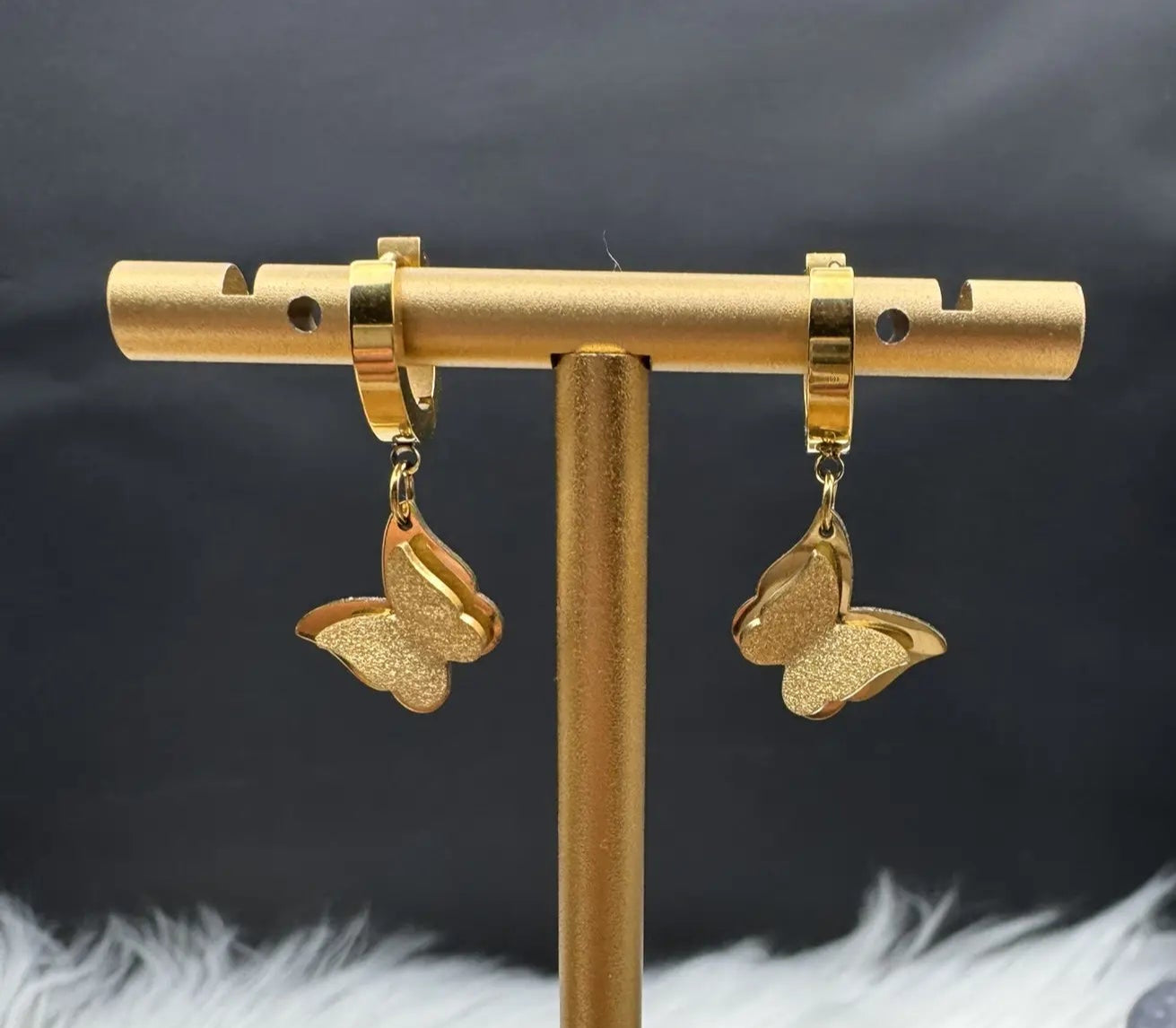 Gold plated butterfly earrings on a gold stand with a black background