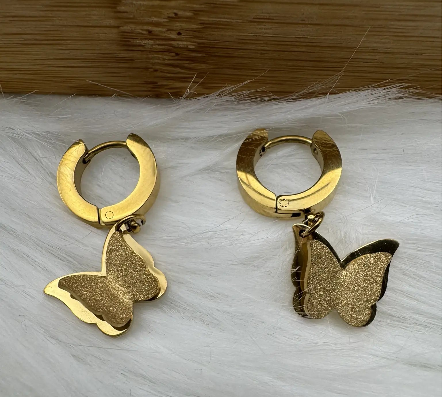 Gold butterfly earrings on a white fur surface with a wooden background