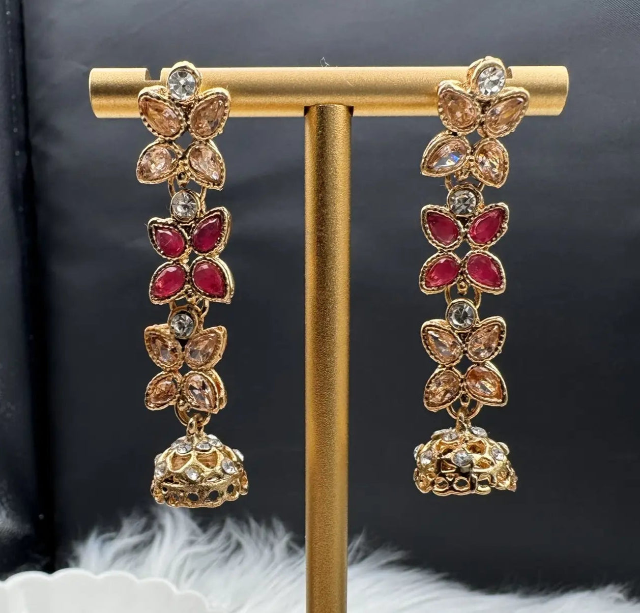 Gold and red floral earrings on a gold stand with a dark background