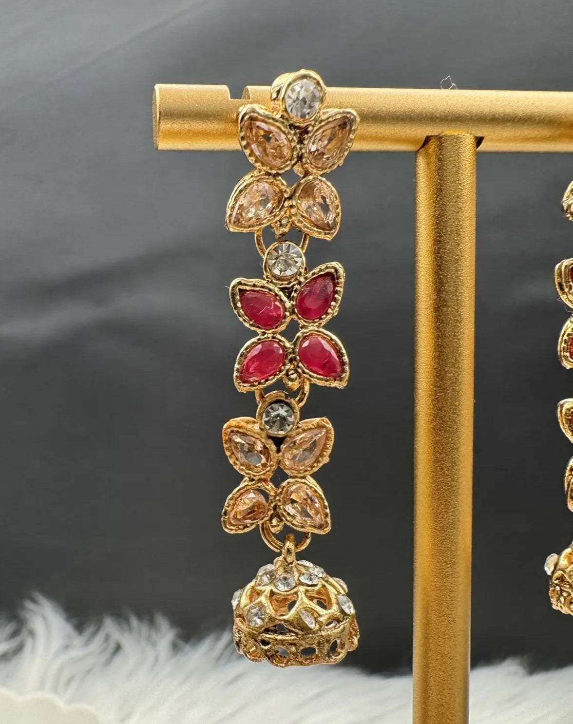 gold plated dangling earrings with a little jhumki at the bottom on a gold stand with a dark background