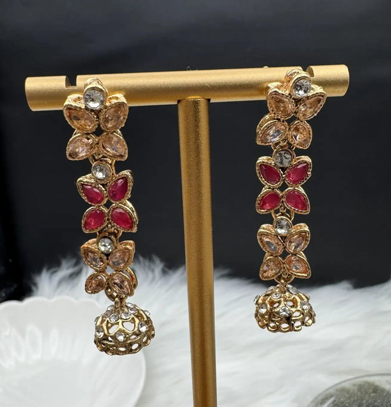 Decorative dangling earrings with a little jhumki at the bottom on a gold stand with a dark background