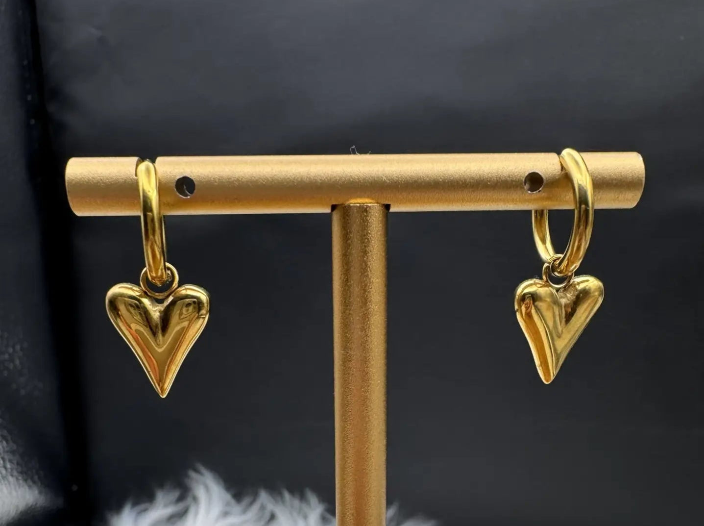 Gold plated and stainless steel small heart shaped hoop earrings with a black background