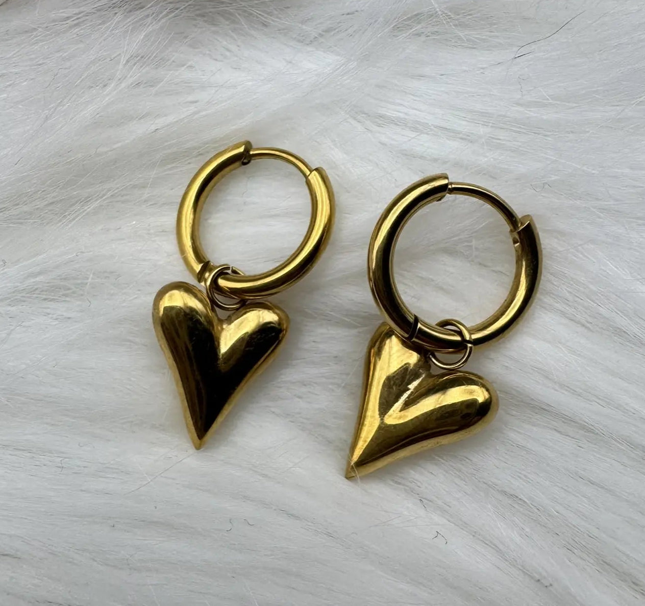 Gold plated and stainless steel small heart shaped hoop earrings on a furry cloth