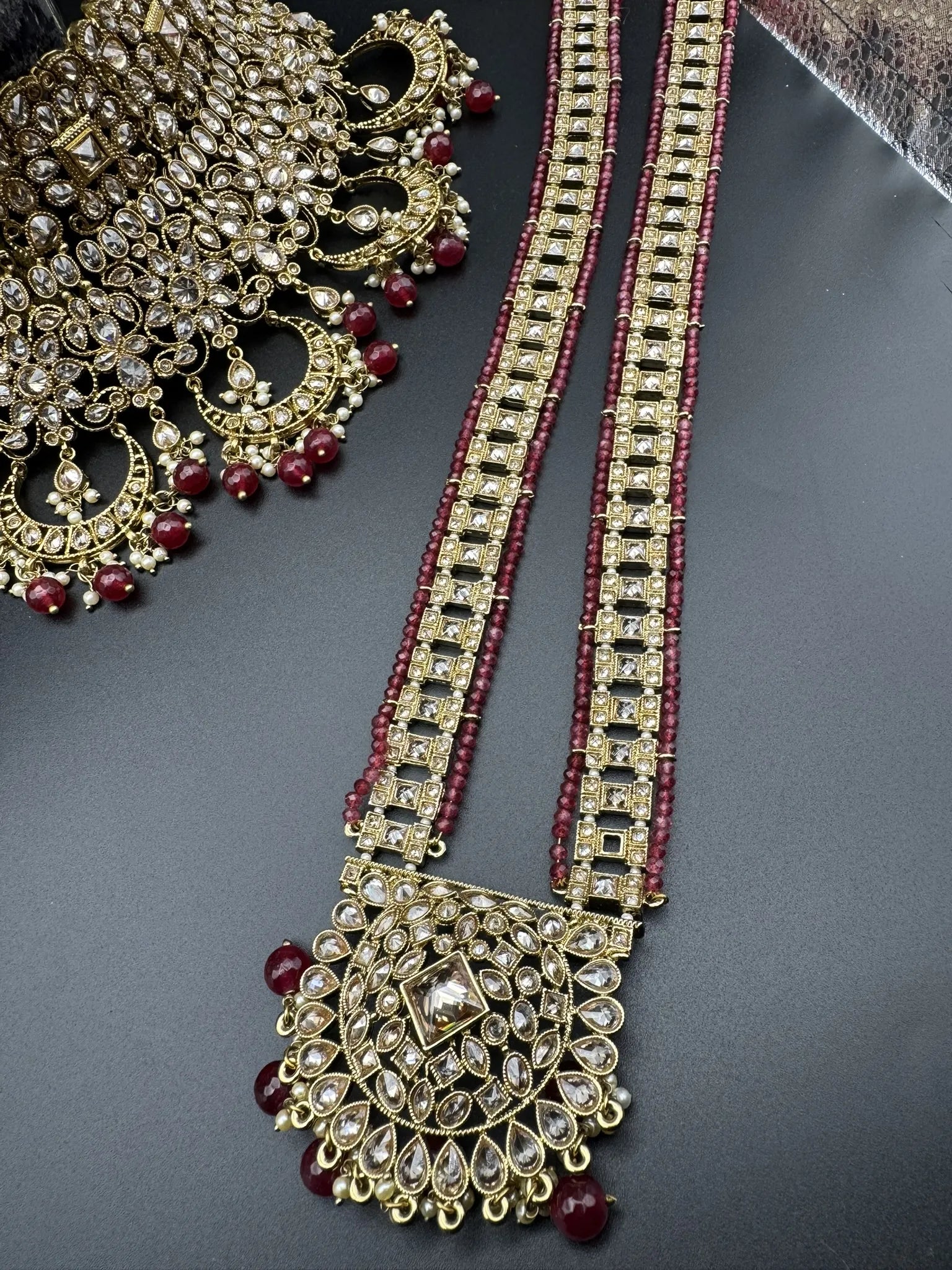 necklace focused view of exquisite gold-plated Indian bridal set with red accents, sparkling stones & matching earrings, teeka and a long traditional necklace. Waterproof & anti-tarnish.