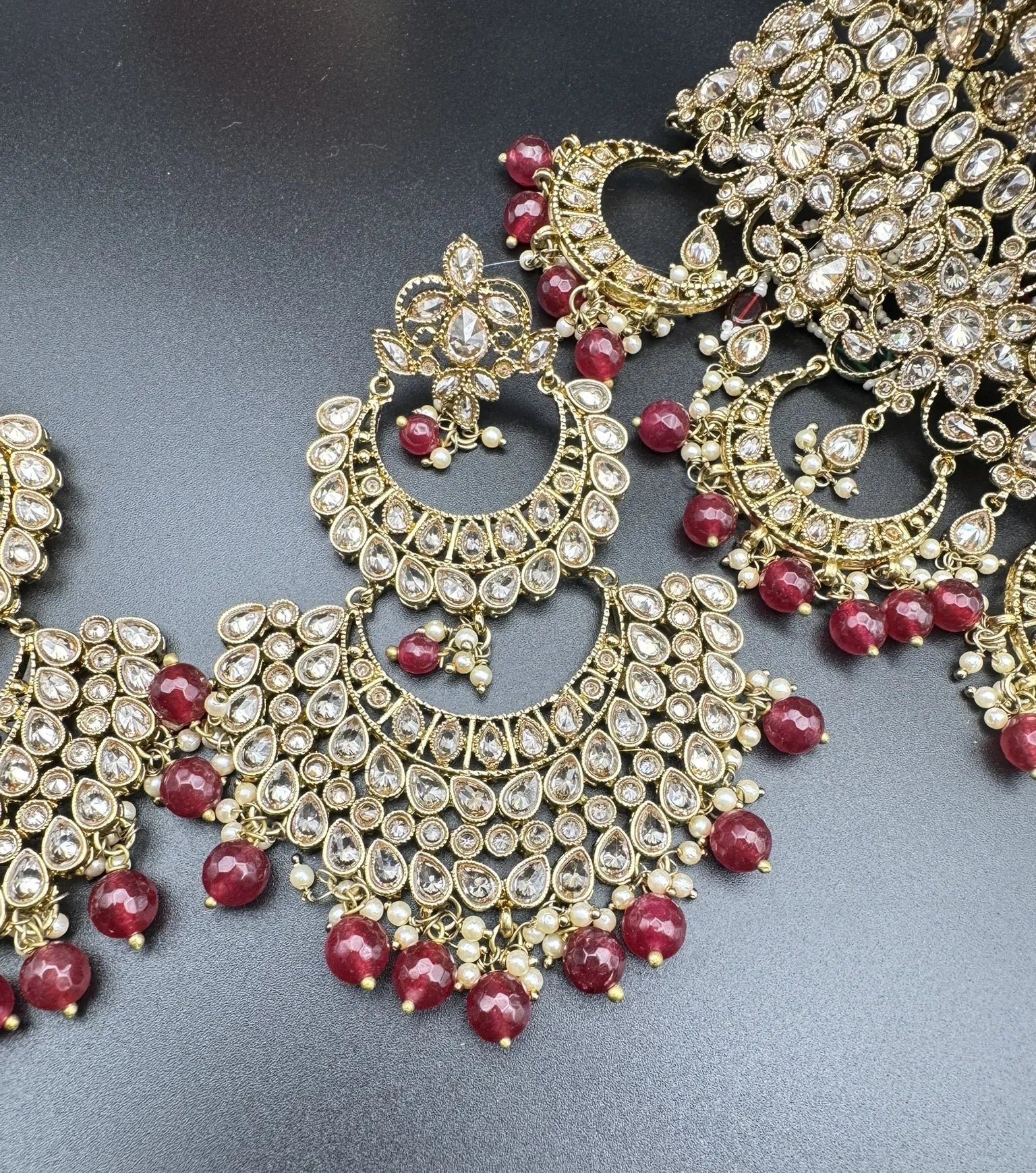 earring focused view of exquisite gold-plated Indian bridal set with red accents, sparkling stones & matching earrings, teeka and a long traditional necklace. Waterproof & anti-tarnish.