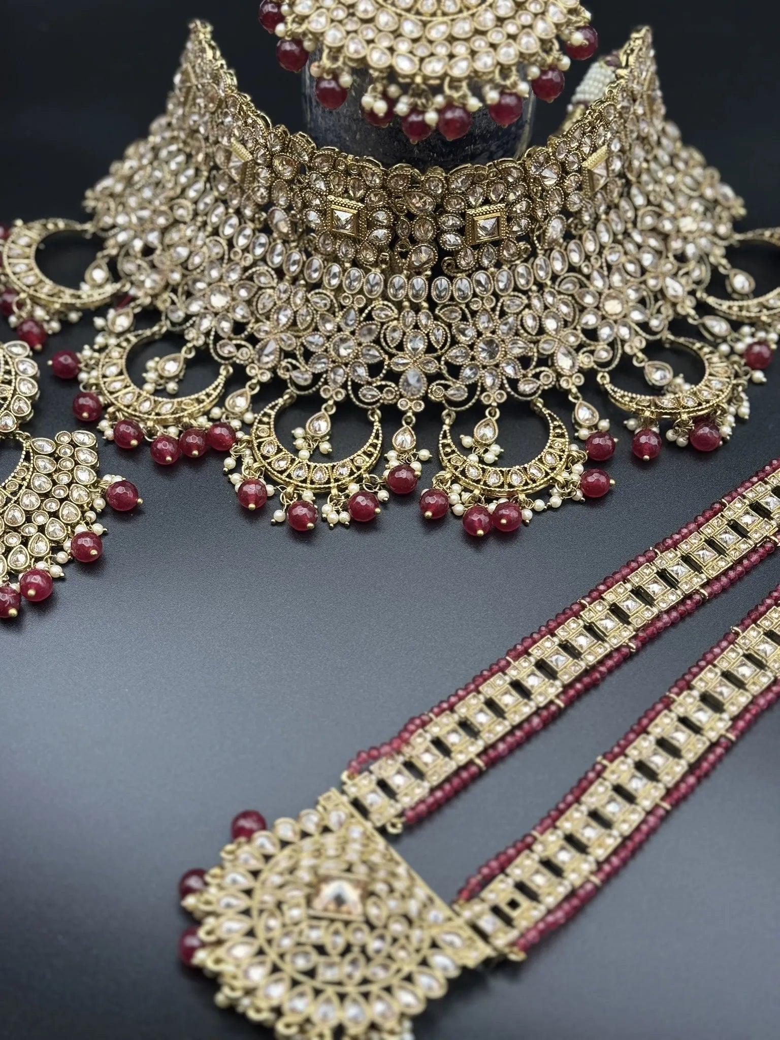 necklace view of exquisite gold-plated Indian bridal set with red accents, sparkling stones & matching earrings, teeka and a long traditional necklace. Waterproof & anti-tarnish.