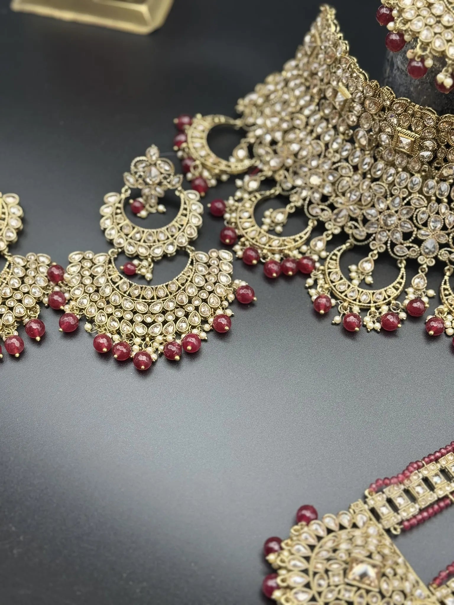 earring focused view of exquisite gold-plated Indian bridal set with red accents, sparkling stones & matching earrings, teeka and a long traditional necklace. Waterproof & anti-tarnish.