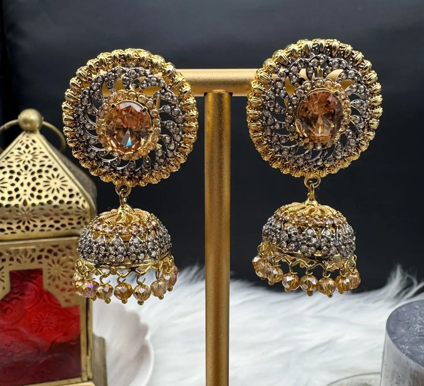 right side view of Pakistani style jhumka earrings gold-plated and champagne colored gemstones on a stand with a dark background