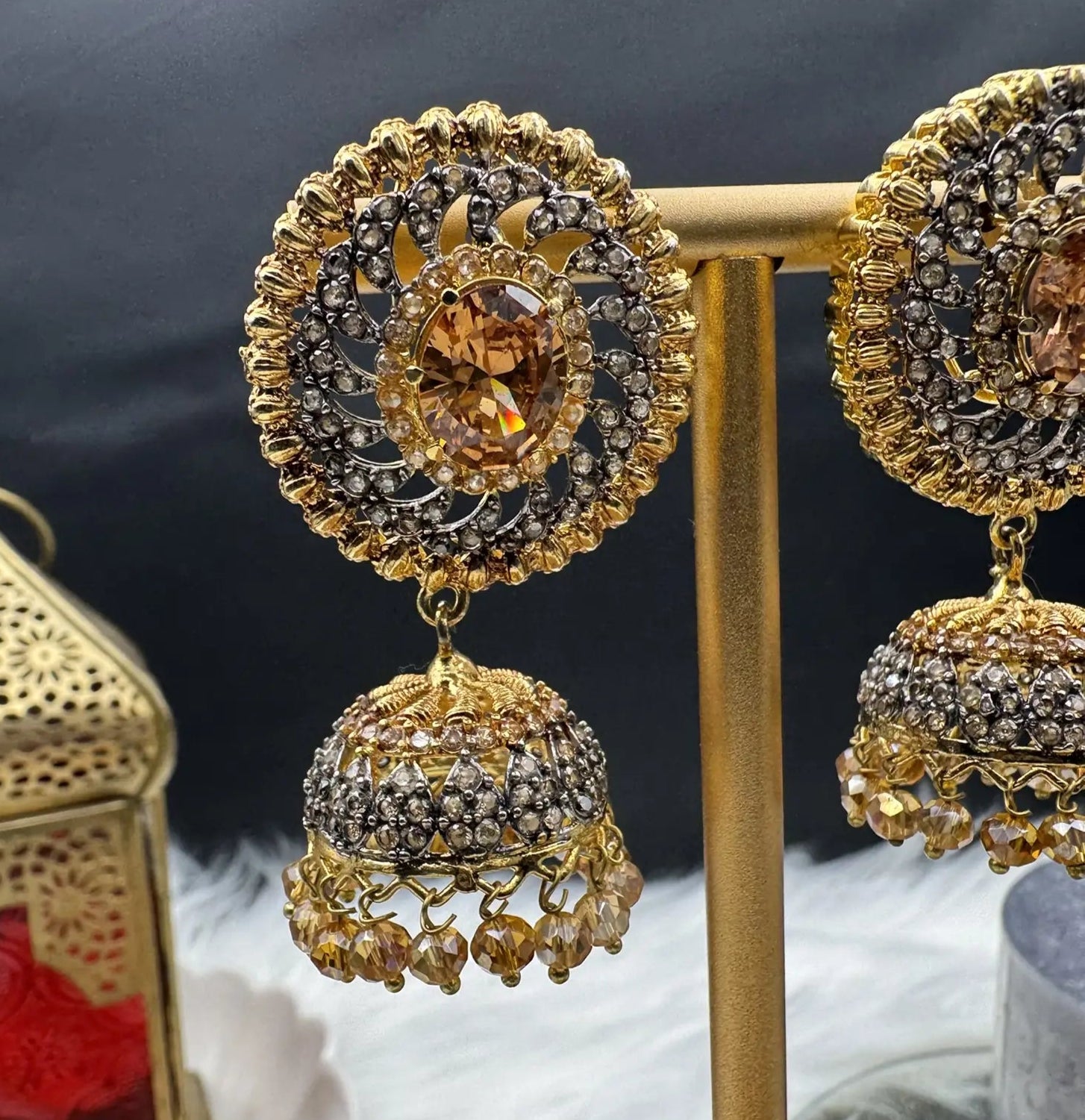 single earring view of Pakistani style jhumka earrings gold-plated and champagne colored gemstones on a stand with a dark background