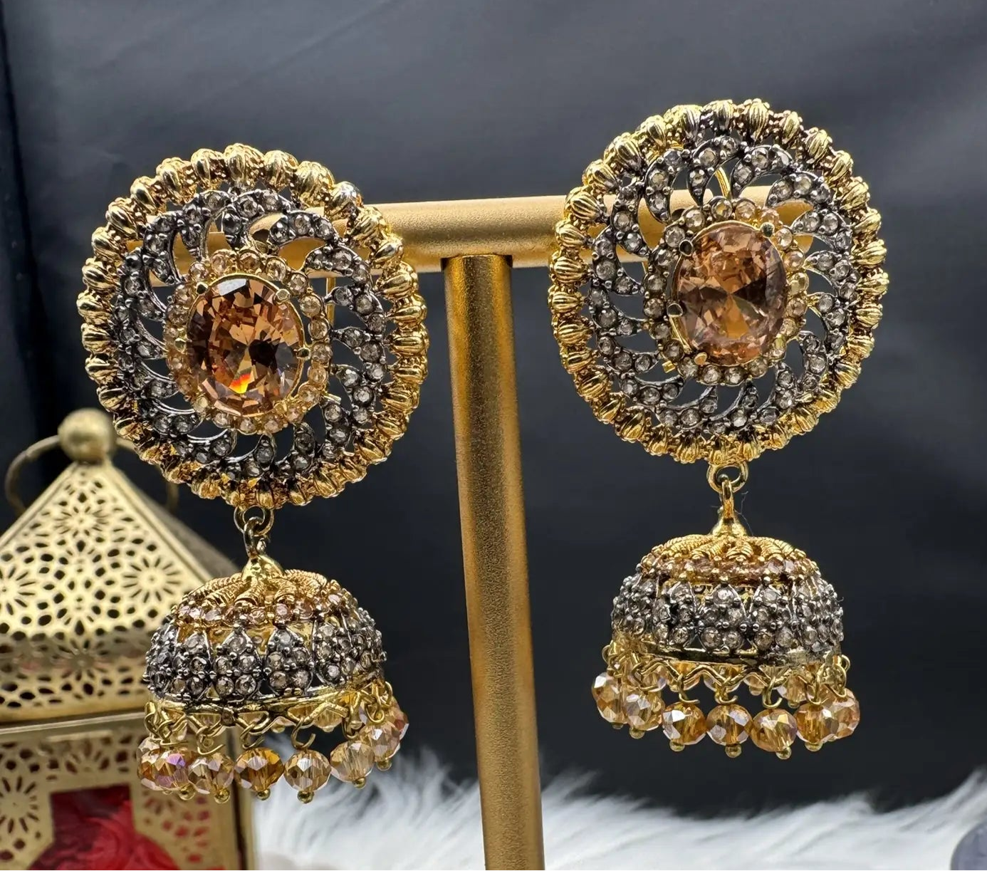 Pakistani style jhumka earrings gold-plated and champagne colored gemstones on a stand with a dark background
