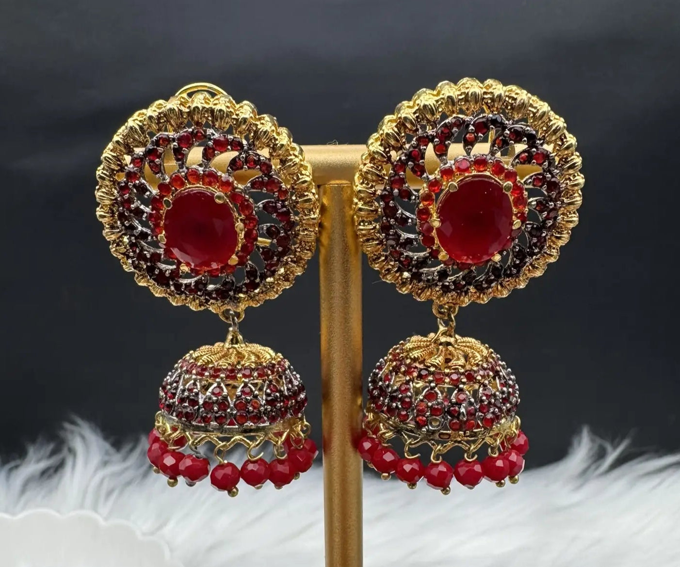 top view of Pakistani style jhumka earrings gold-plated and red colored gemstones on a stand with a dark background