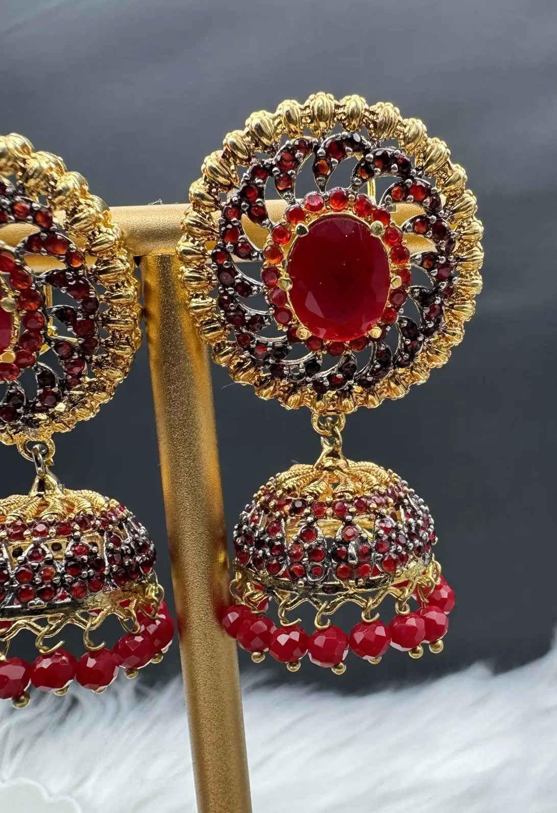 Pakistani style jhumka earrings gold-plated and red colored gemstones on a stand with a dark background