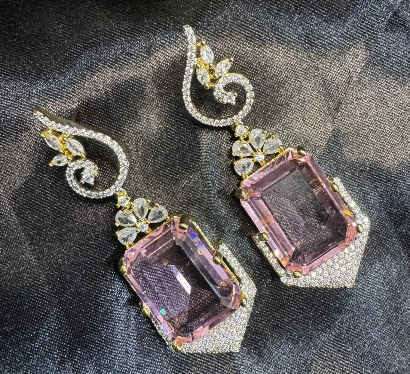 Pair of earrings with pink and clear gemstones on a dark fabric background