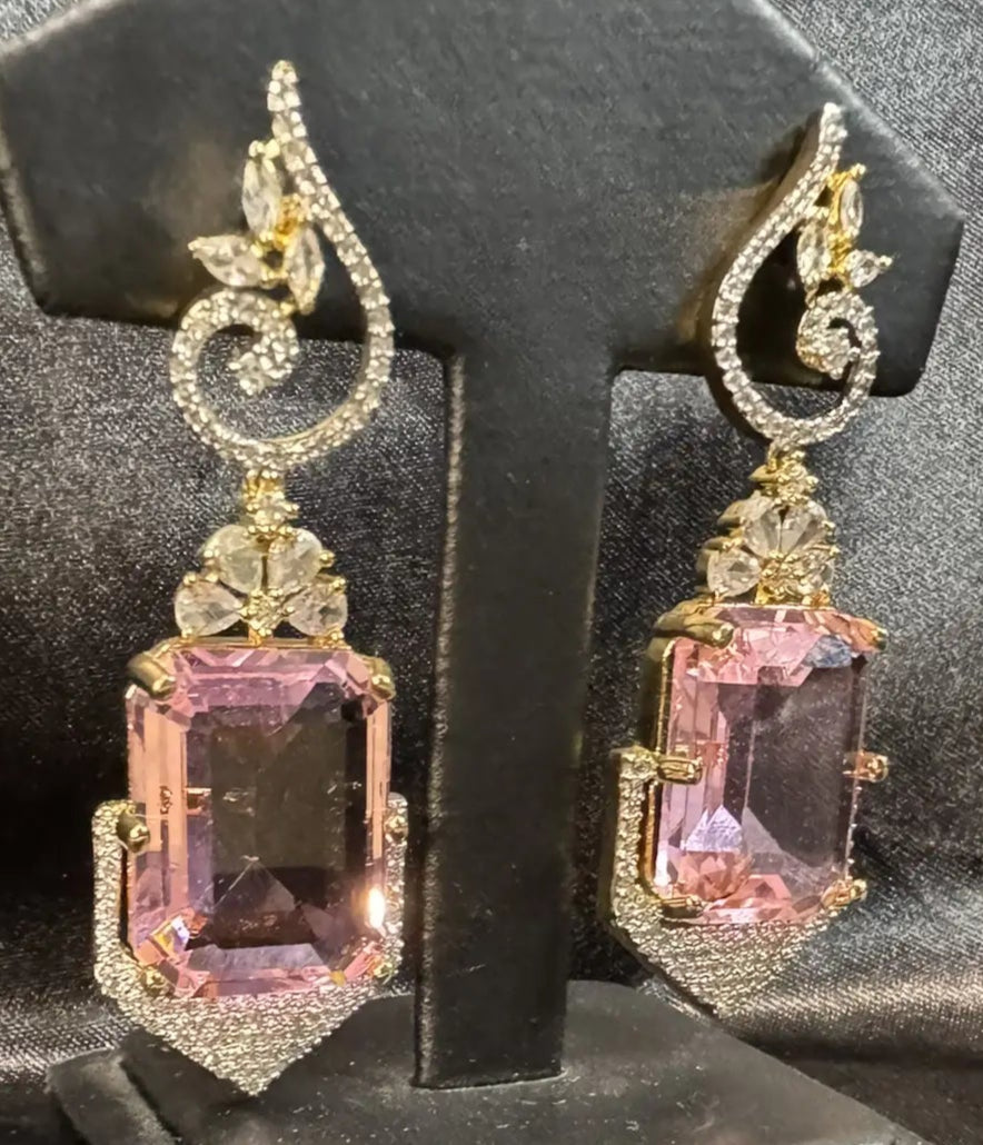 Pair of ornate earrings with pink gemstones on a black stand against a dark background