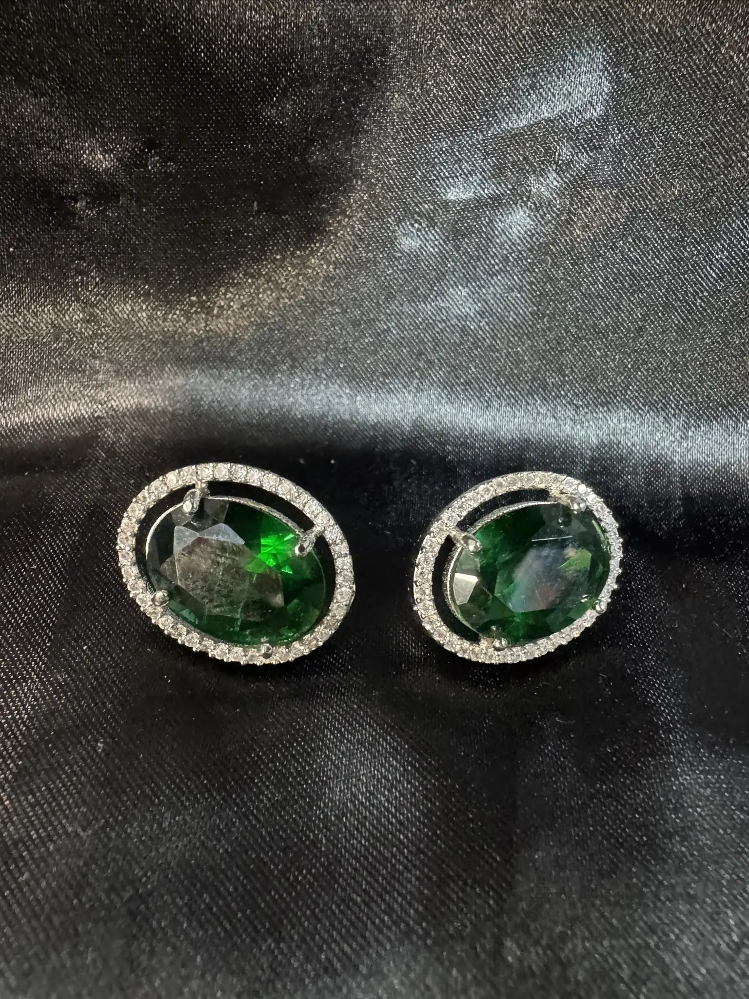 Pair of green gemstone earrings on a black fabric background