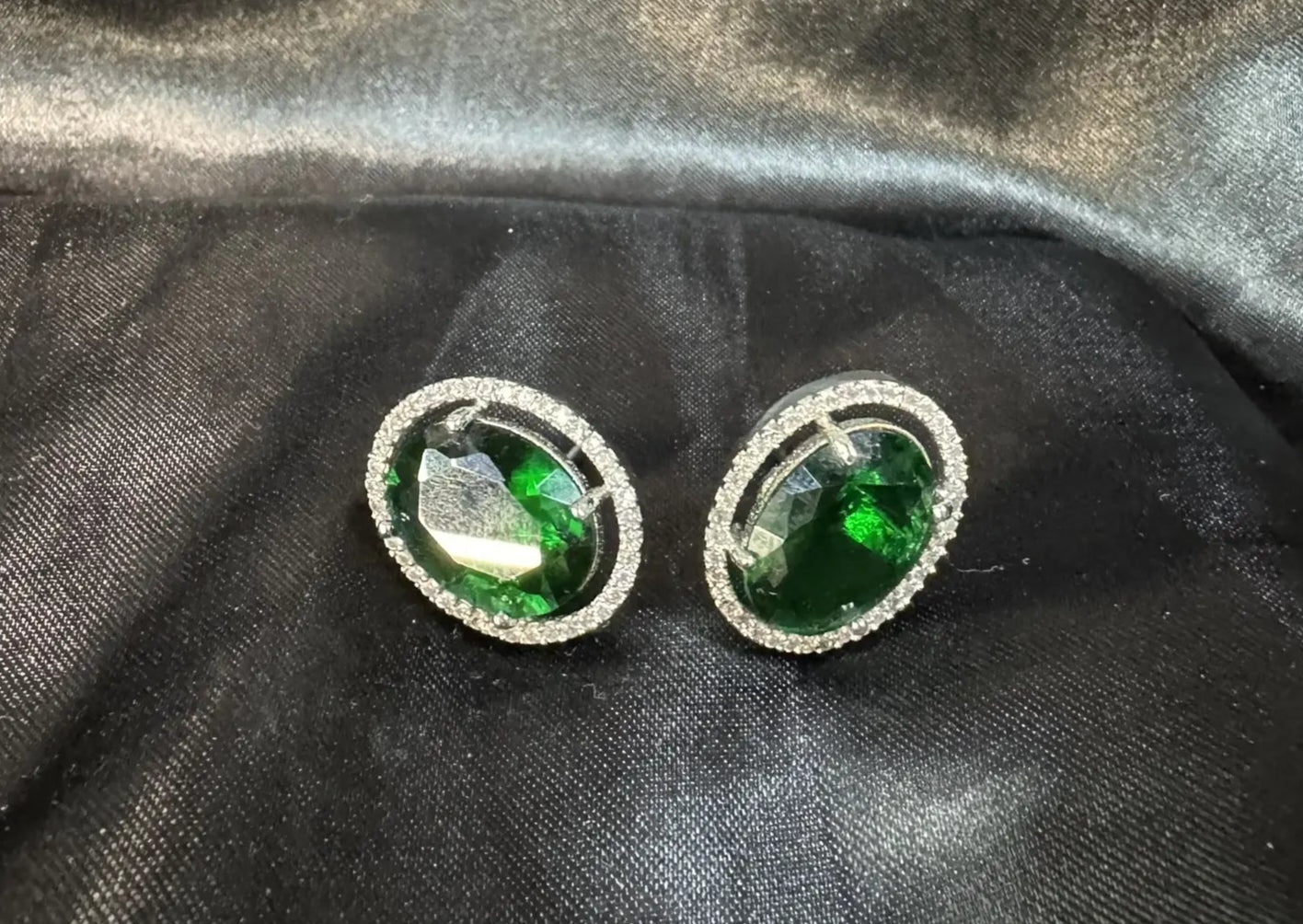 Pair of stud earrings with green gemstones on a black satin background