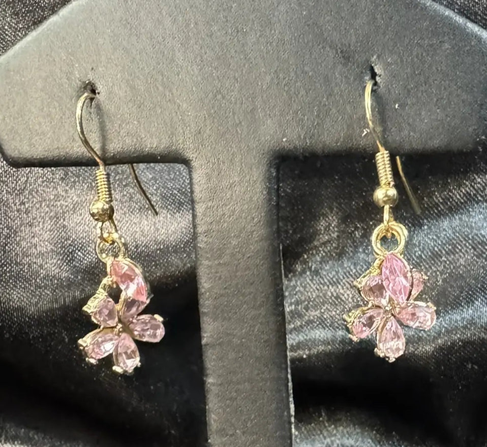 Pair of pink flower earrings on a black earring stand against a black background