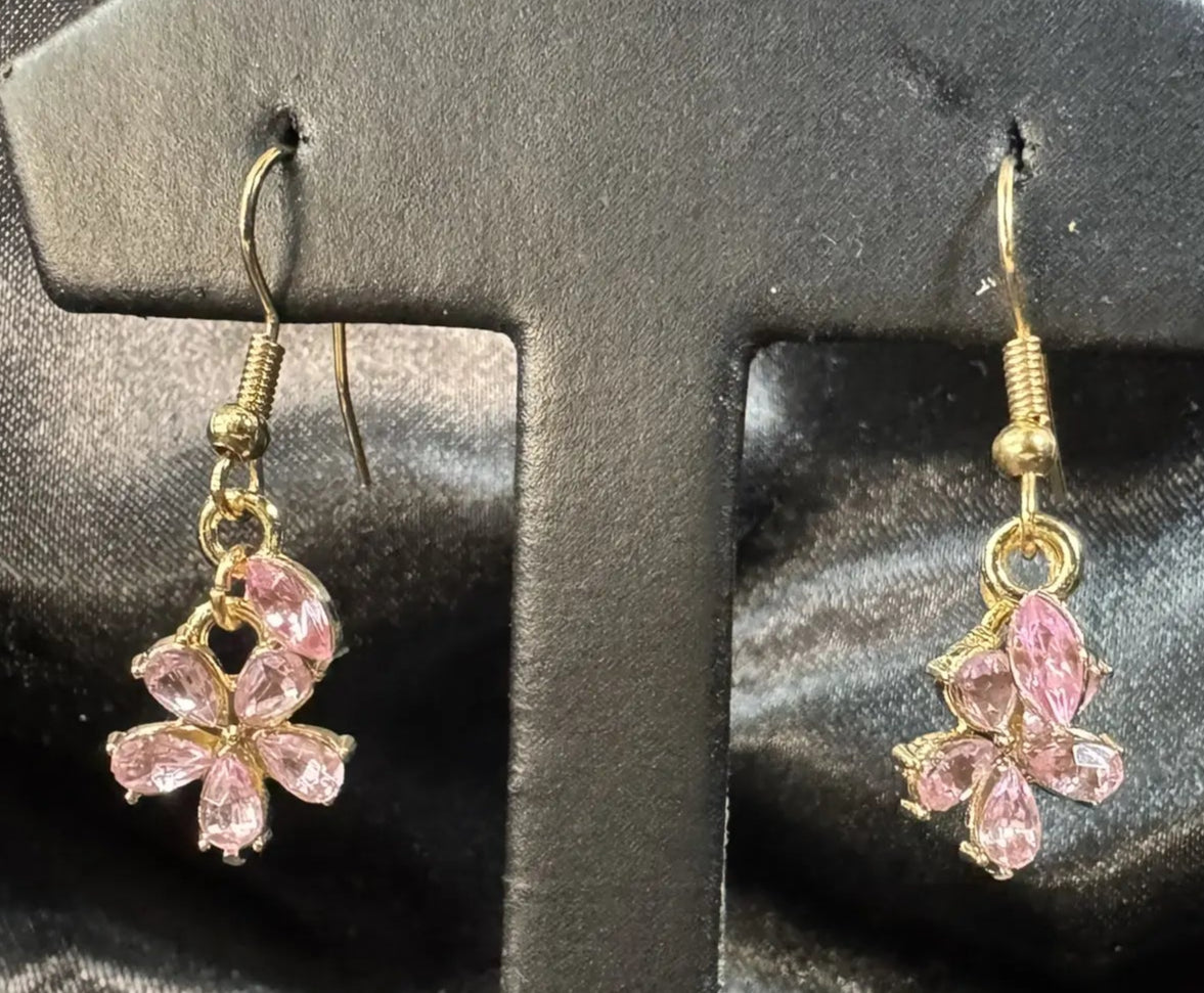Pink flower-shaped earrings on a black earring stand against a black satin background