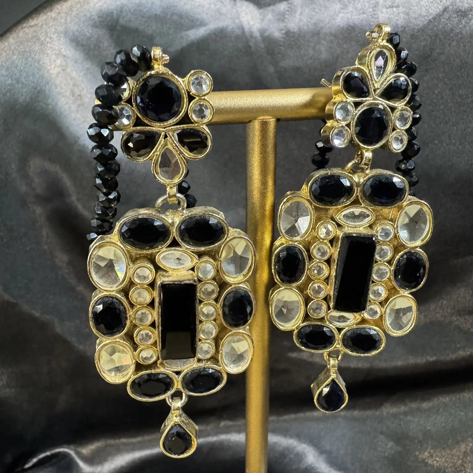 Ornate earrings with black and gold design on a dark fabric background