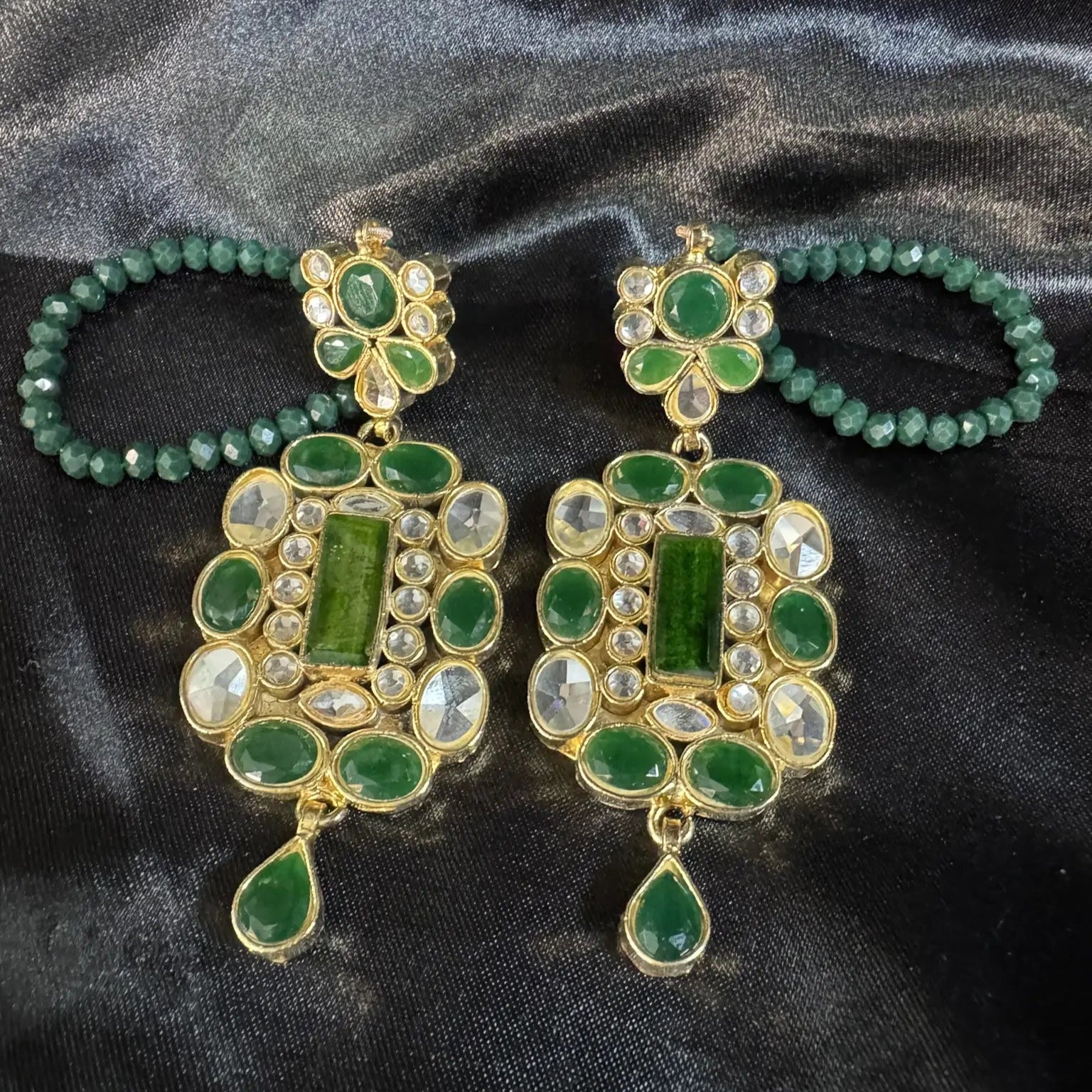 Pair of green and gold earrings on a black satin background