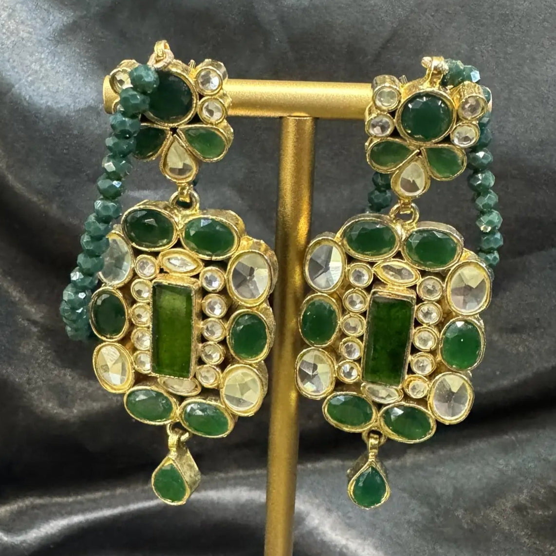 Green and gold earrings on a black satin background