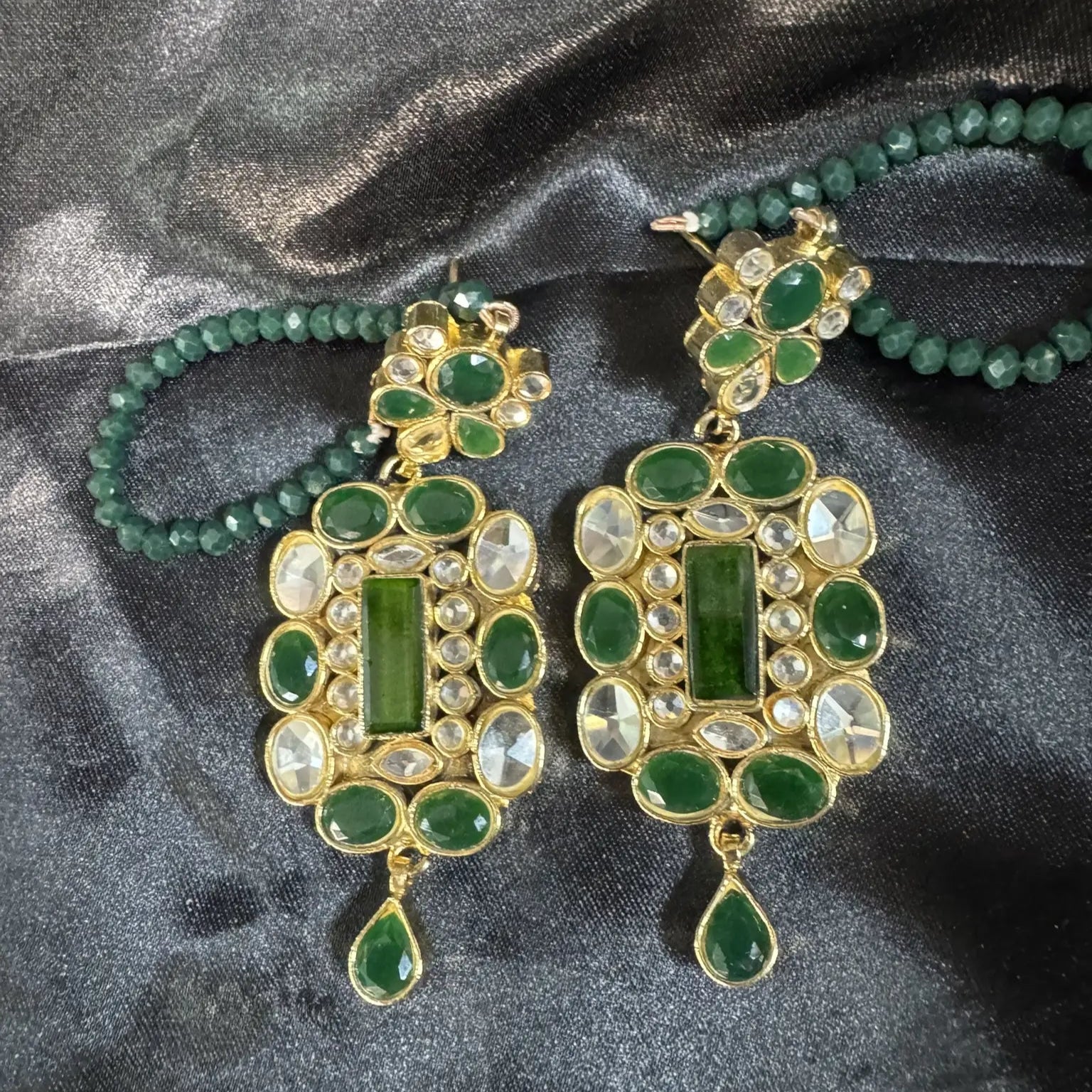 Pair of green and gold earrings on a dark fabric background