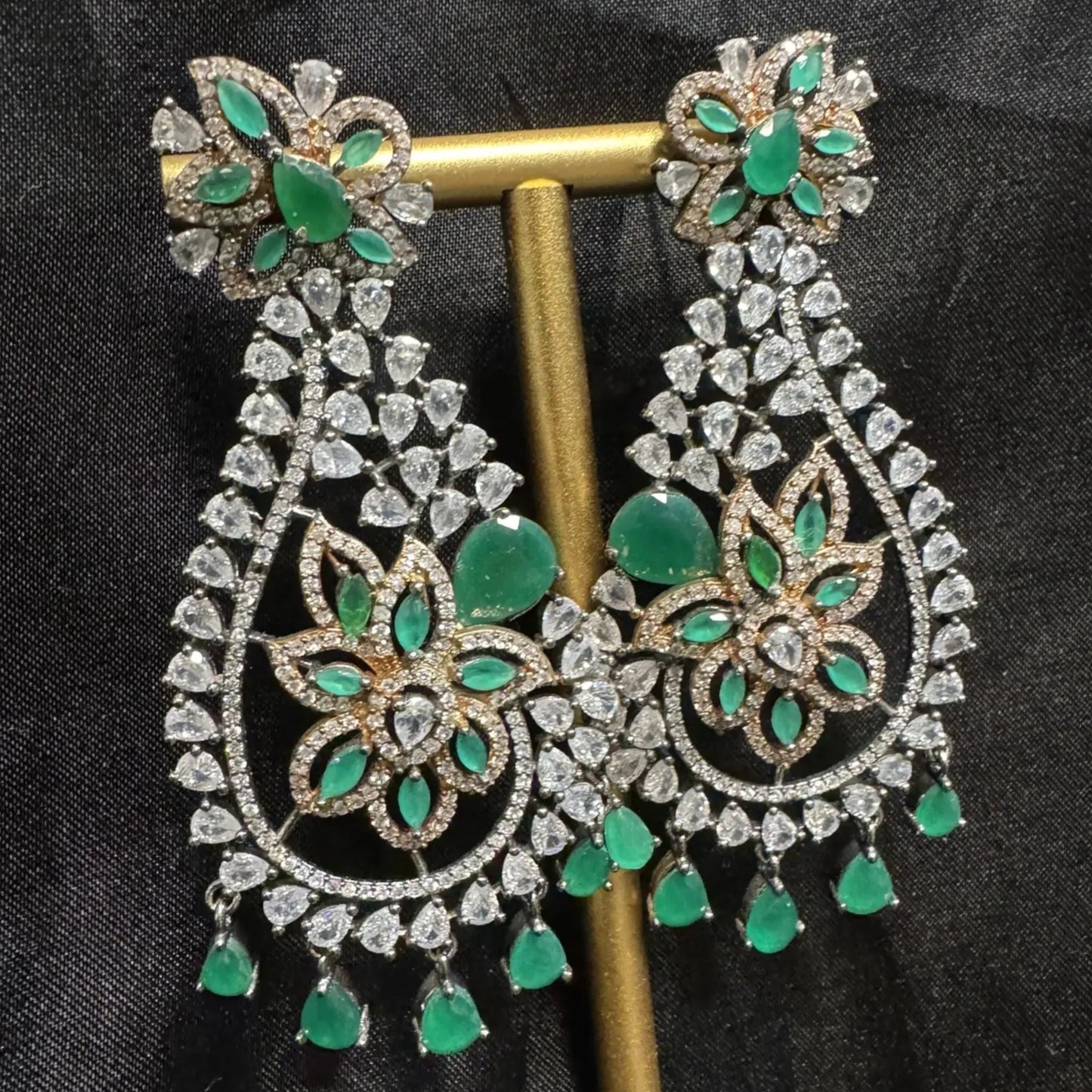 Pair of ornate earrings with green gemstones on a black background