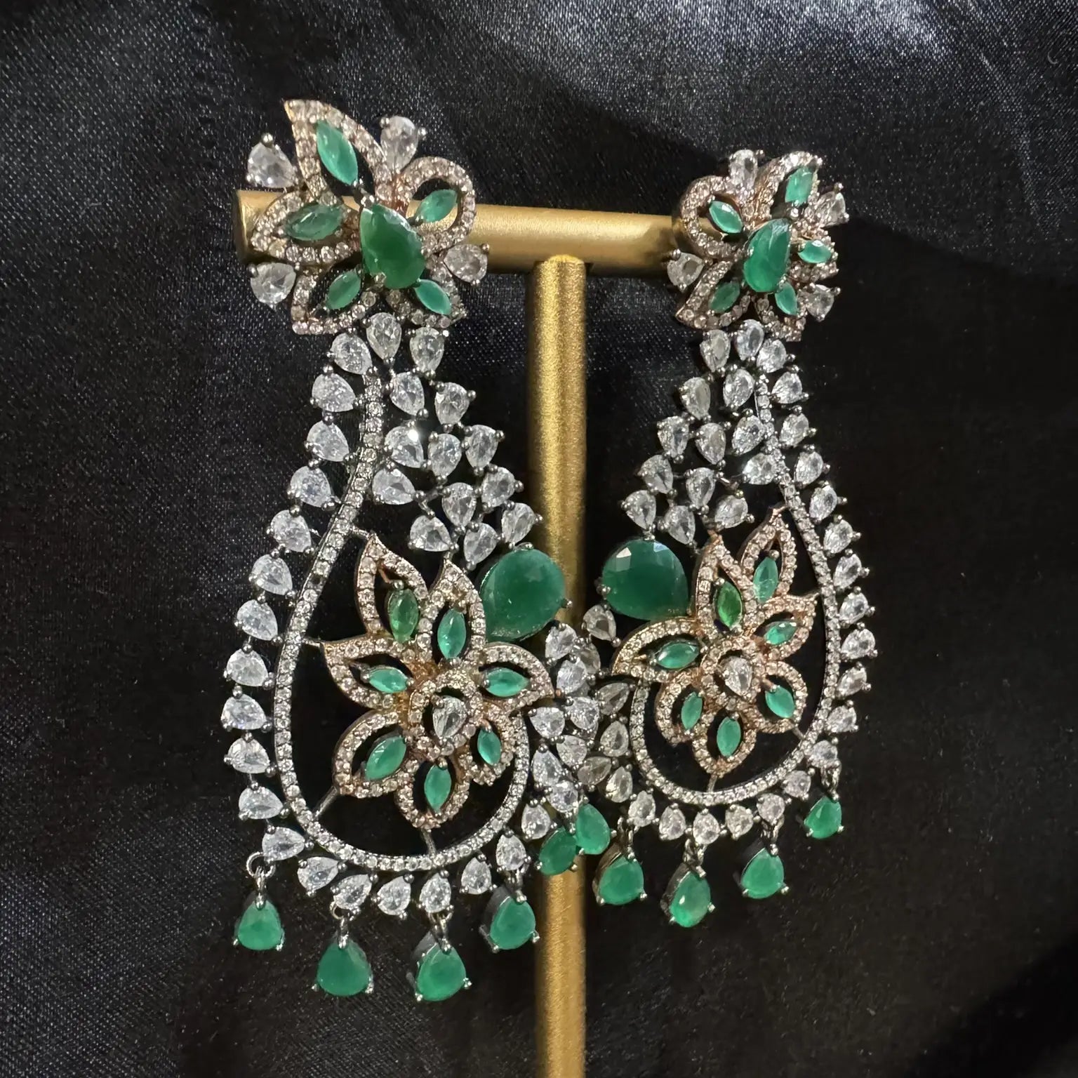 Ornate earrings with green gemstones on a black background