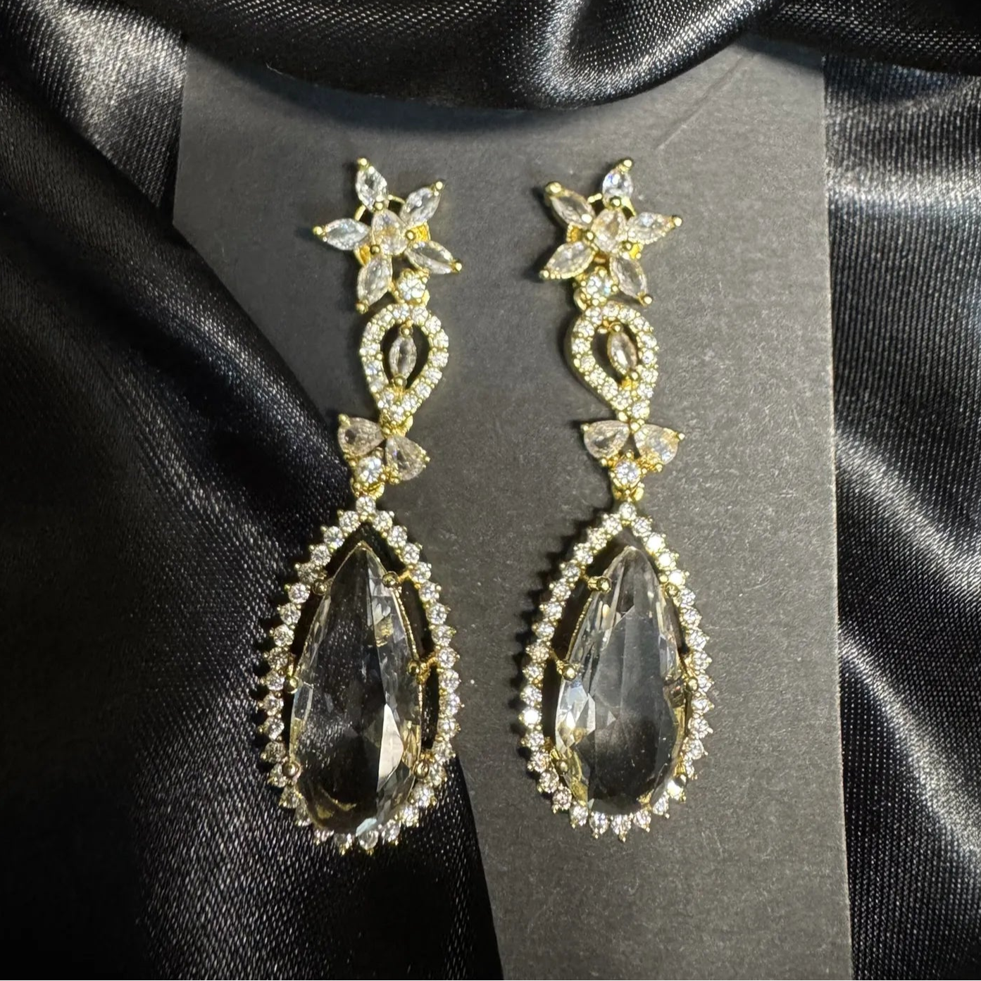 Pair of gold and clear teardrop earrings with American diamonds on a black satin background