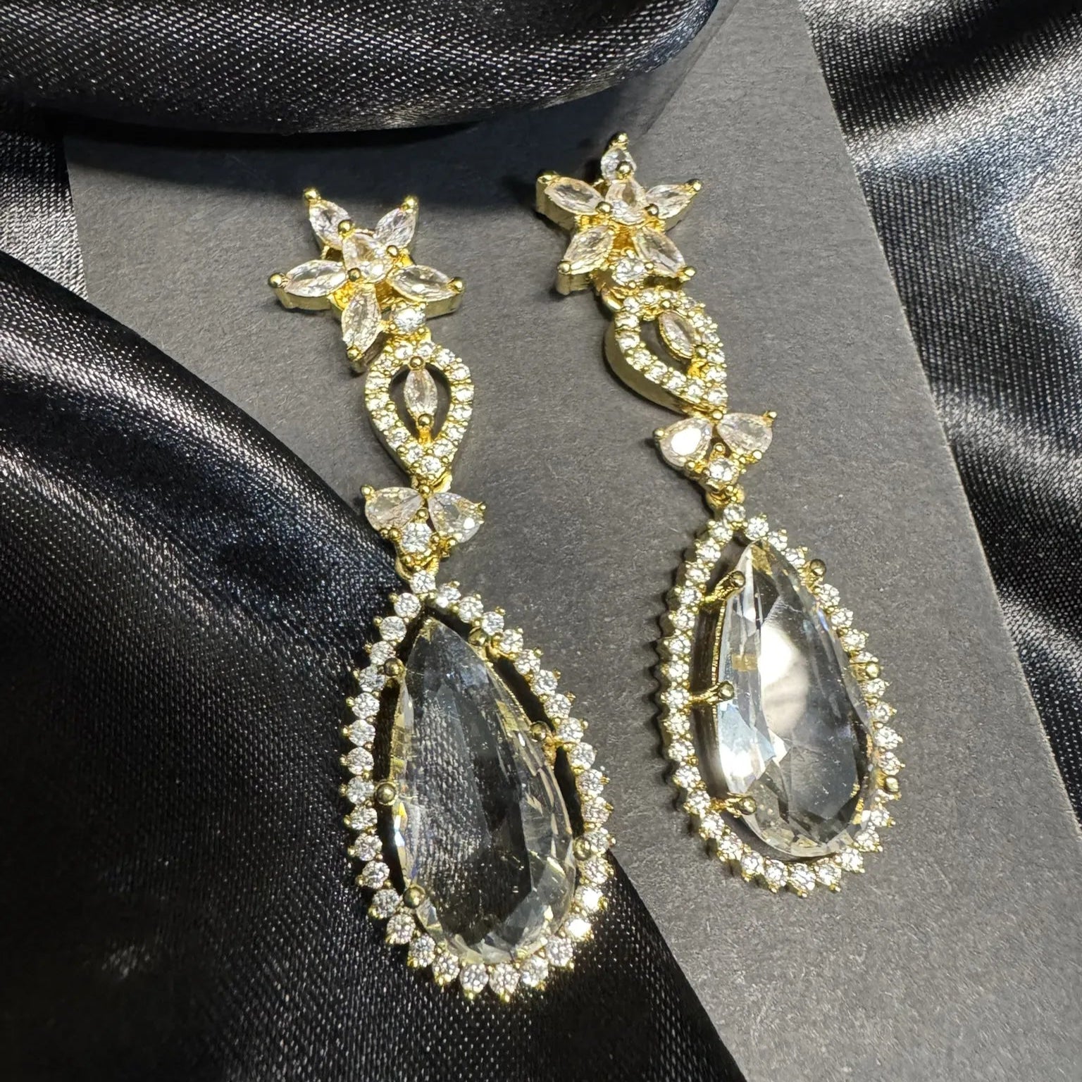 Gold and clear teardrop earrings with American diamonds on a black satin background