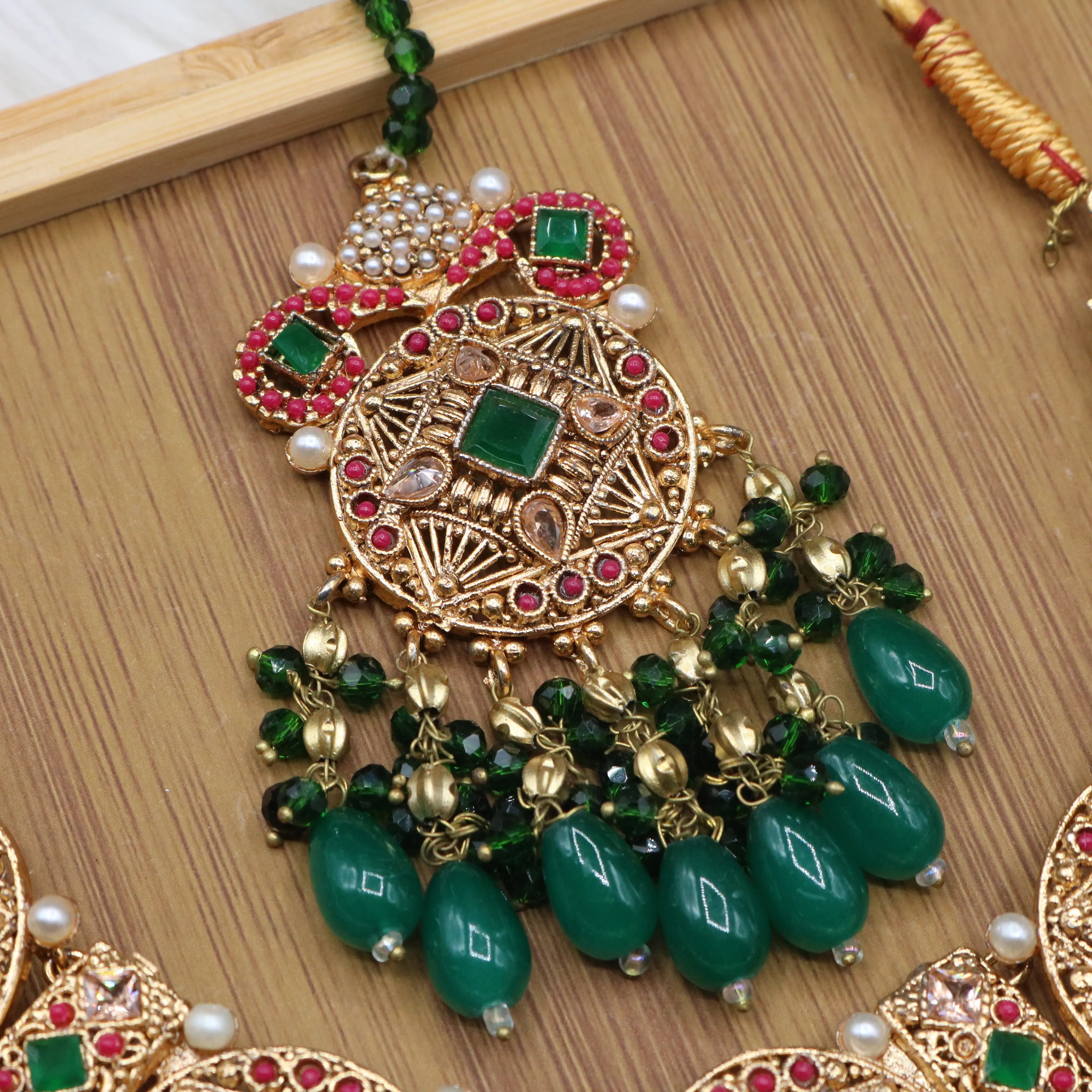 Teeka view of Pakistani bridal set handcrafted with intricate gold-plated detailing, this traditional jewelry set features red stone inlays, sparkling accents, and rich green bead drops