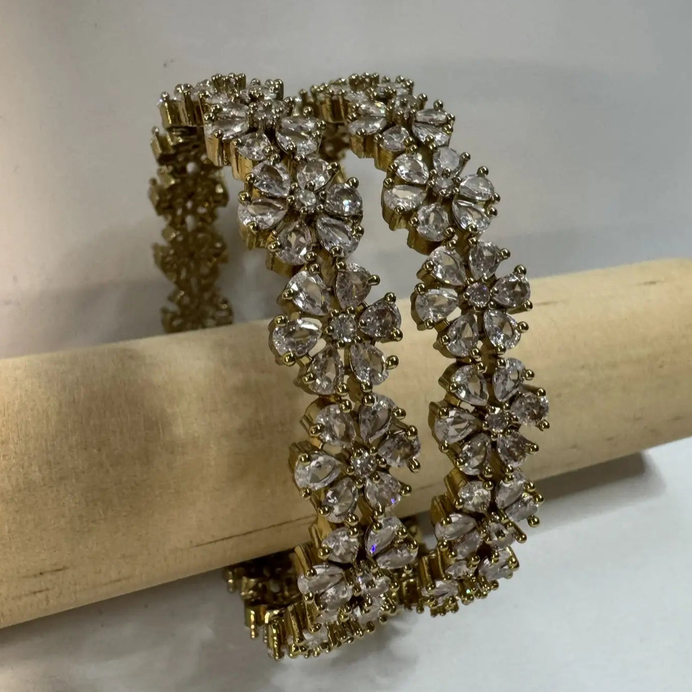 24k gold plated floral pattern bangle set with antique polish for a lasting shine on a wooden stick against a white background