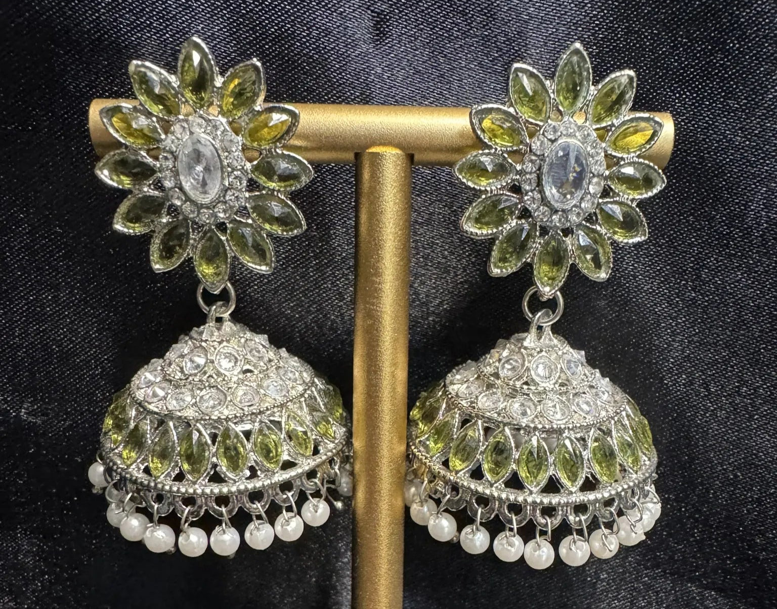 Pair of floral earrings with olive green stones and pearl accents on a black background
