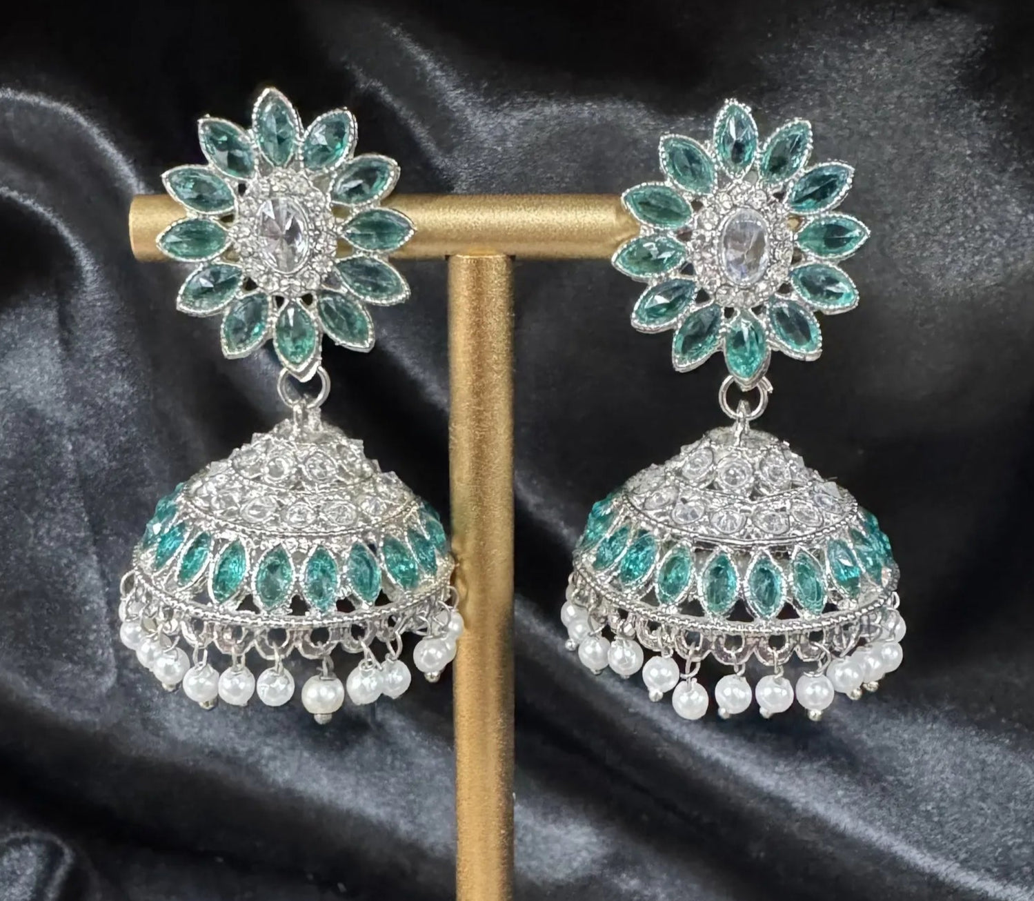 Ornate earrings with teal gemstones and pearl accents on a dark fabric background