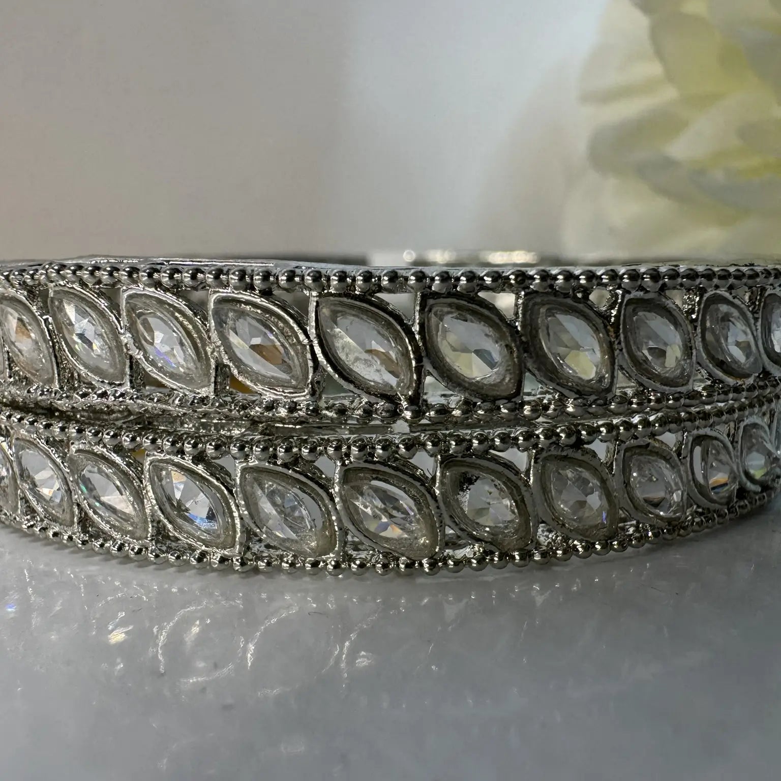 Silver bangles with clear gemstones on a reflective surface