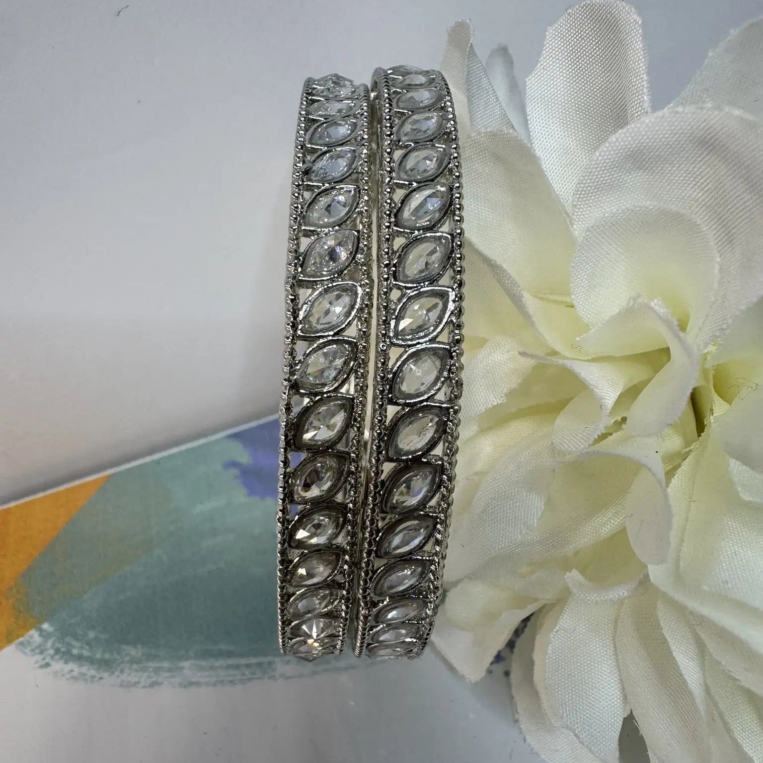 Silver bangles with gemstones on a white surface with a white flower