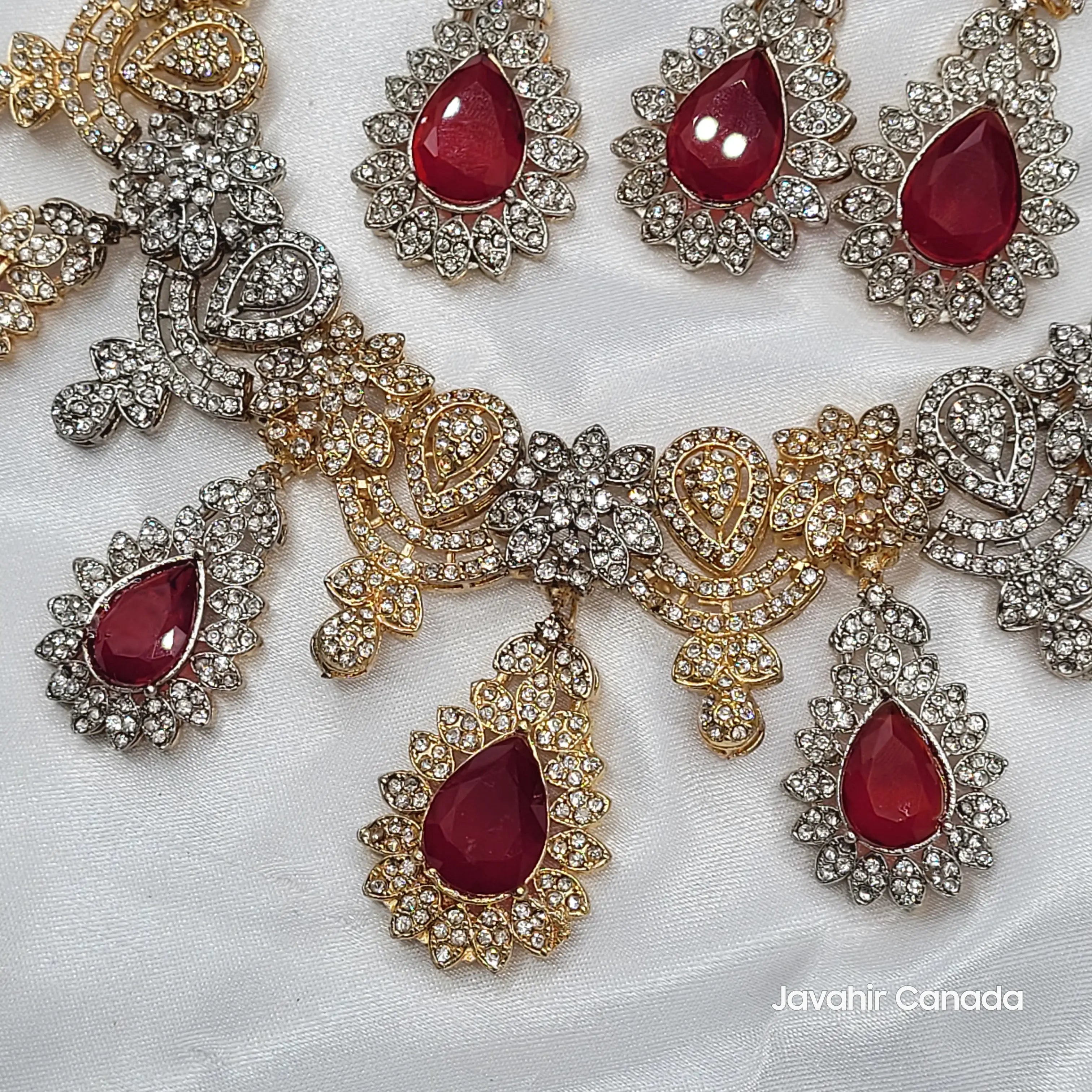 Close-up of JV155 necklace pendant and earrings showing ruby red teardrop stones surrounded by CZ in dual-tone gold and silver finish.