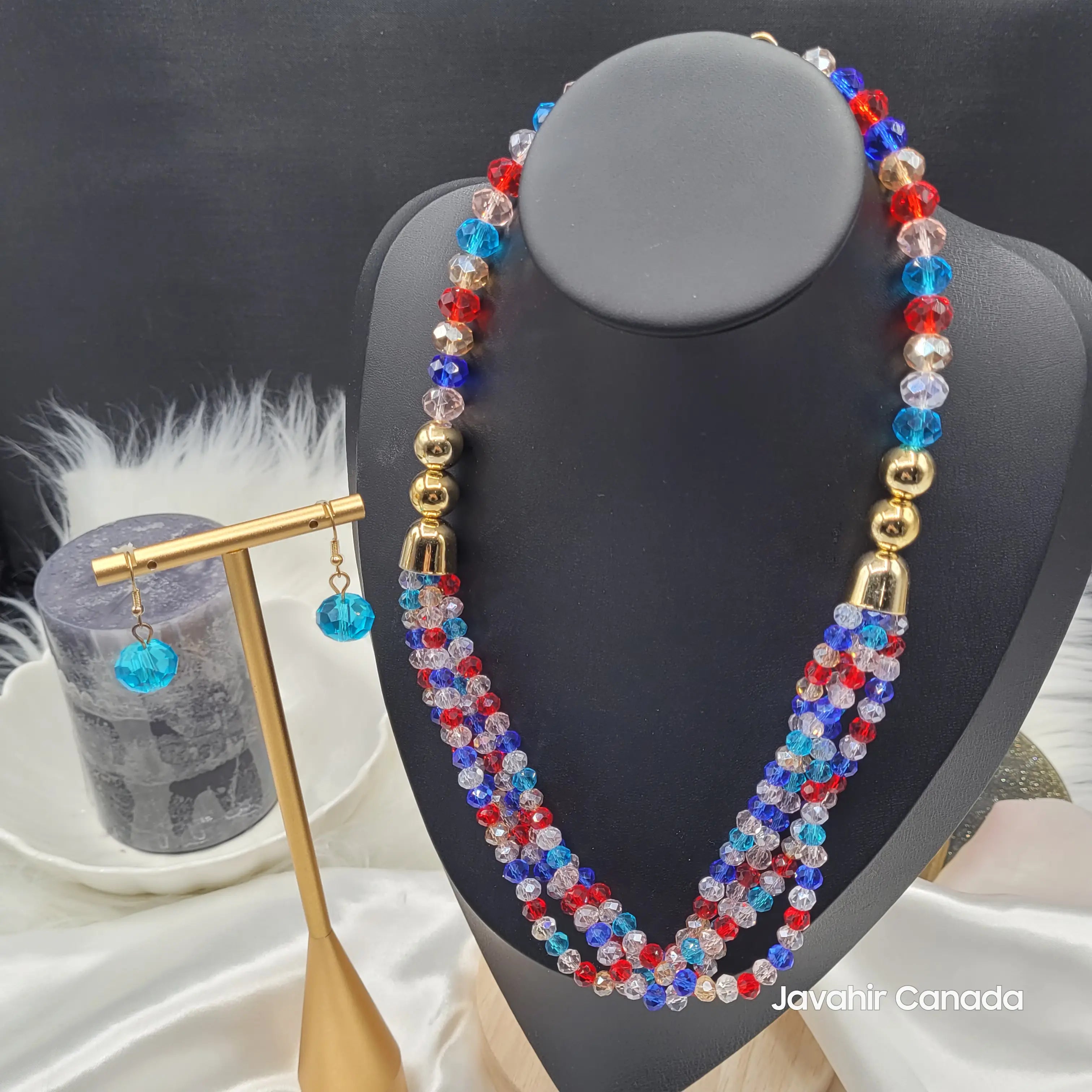 JV161 necklace in a bold red, blue, and clear crystal bead mix, arranged in three twisted layers with golden spacers. Coordinating earrings displayed alongside the set on a black bust.