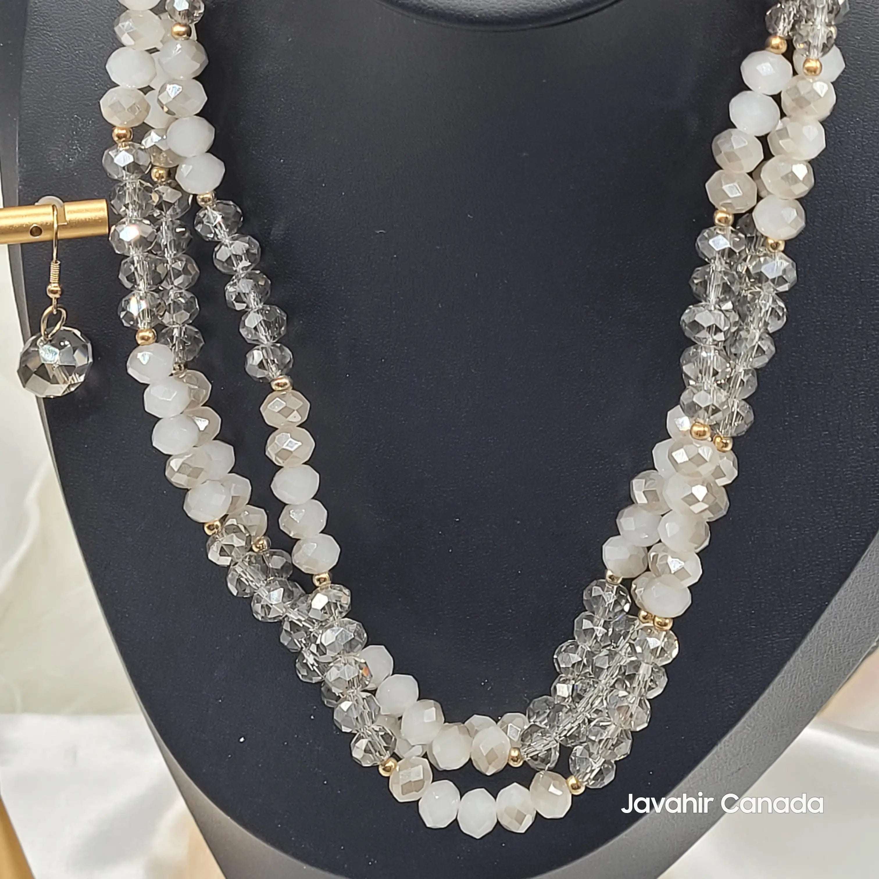 Angled view of the JV161 necklace in smoky grey and white crystal beads. The elegant combination is paired with gold spacers and a matching crystal earring on a gold stand.