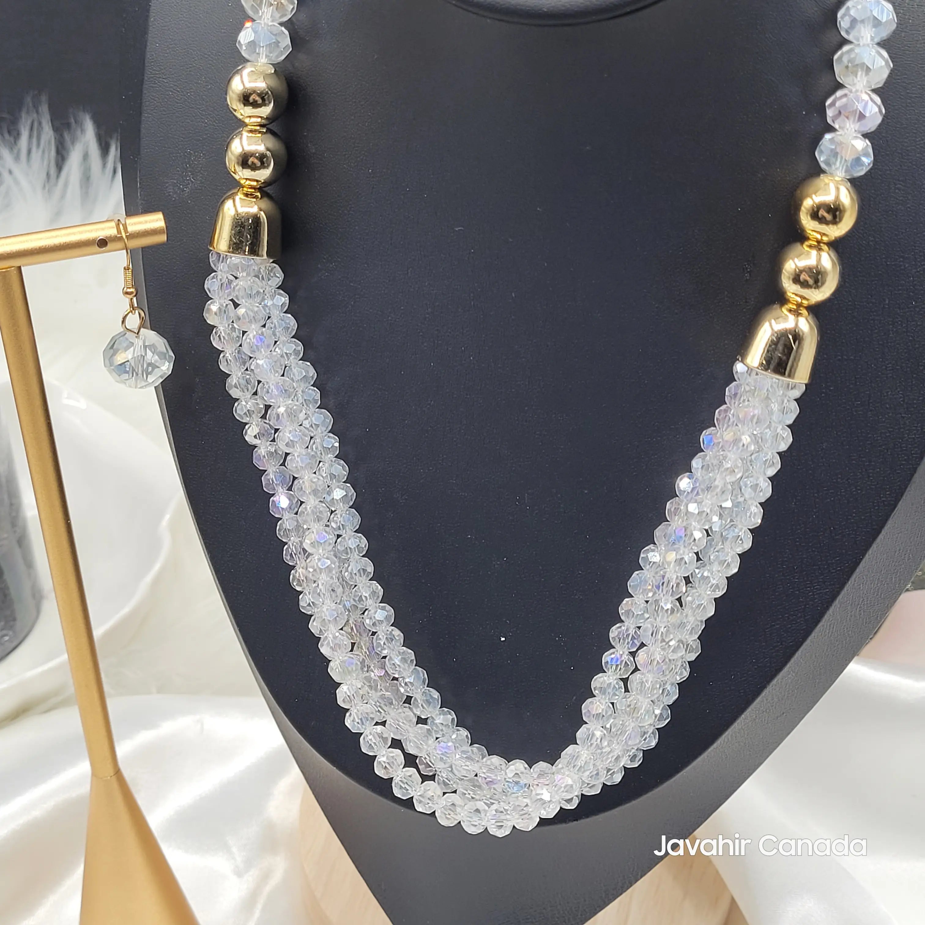 Close-up view of the clear crystal JV161 necklace, highlighting the sparkling beads and twisted triple-strand structure with gold accents. Matching clear earring in focus.