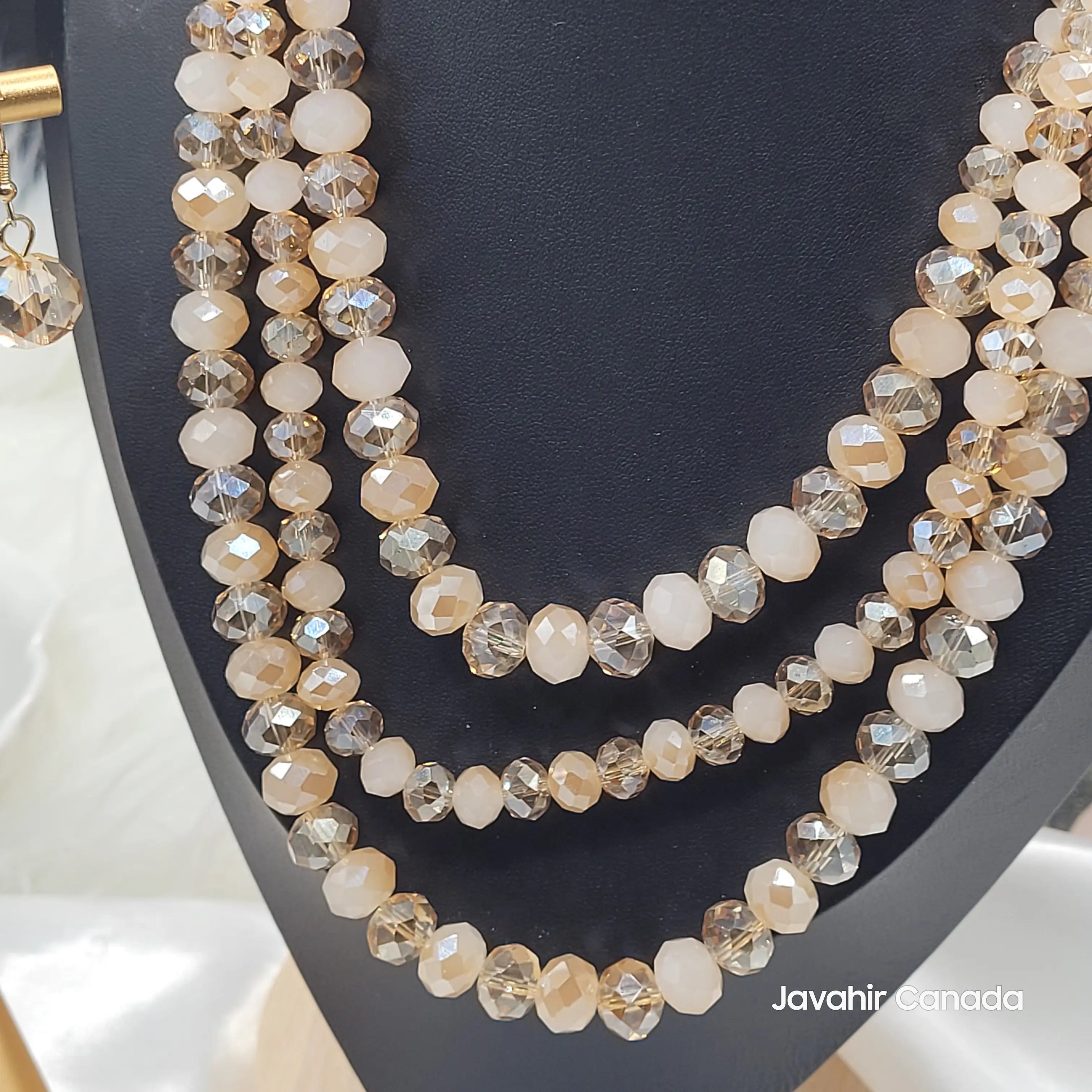 Close-up of the JV162 necklace in a soft champagne beige tone with glossy faceted beads, layered in four strands and paired with a matching beige crystal earring.